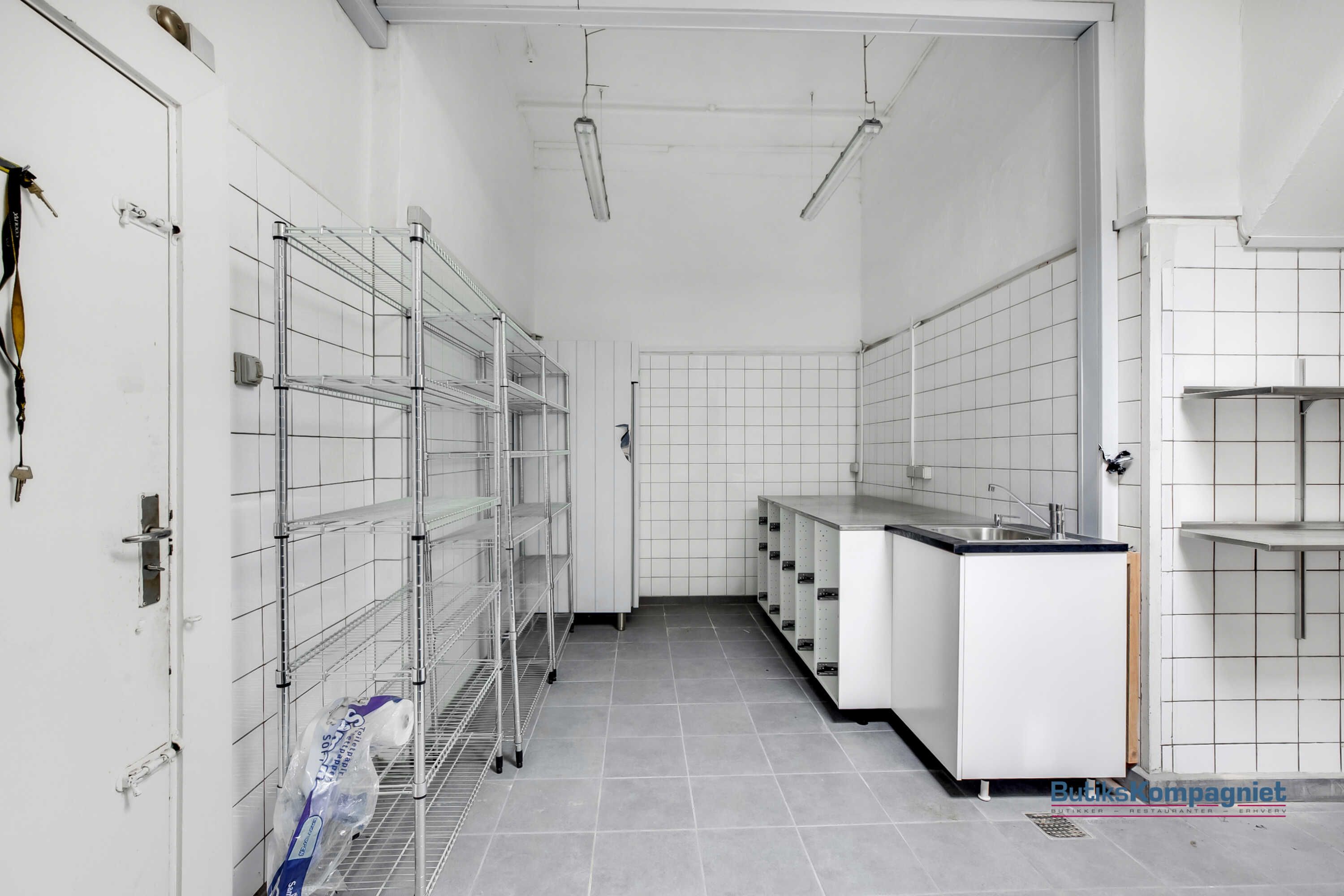 Takeaway-lokaler med højt gulv, hvide vægge og loft, moderne lysekroner, et lagersystem og et nyt køkken med en vaskebækken