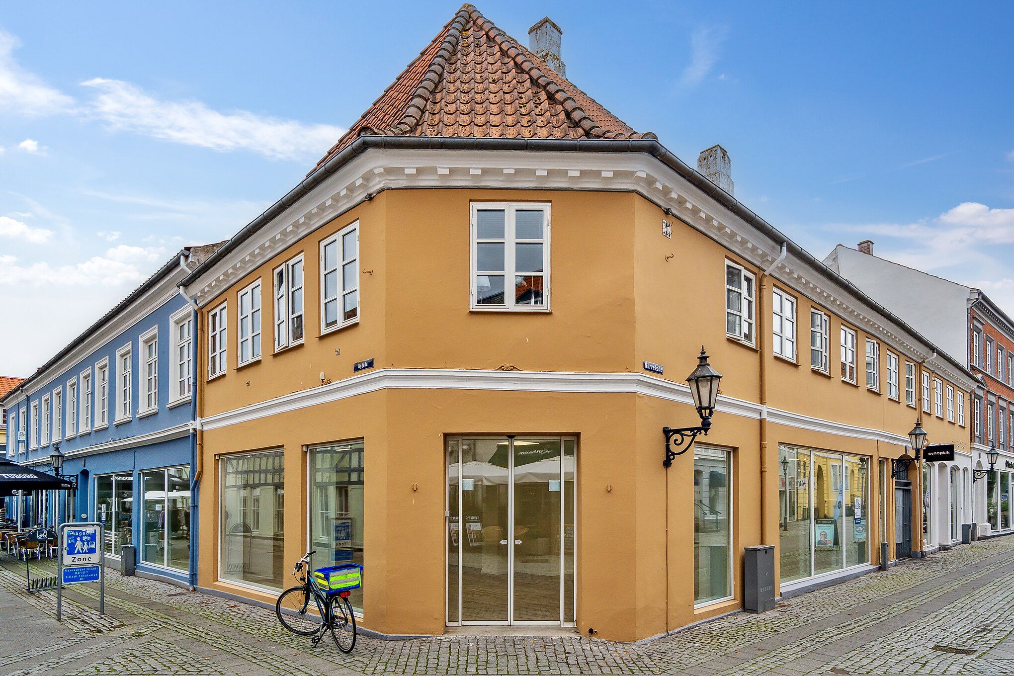 En gammel gul bygning med store glasruder og to butikker. En cykel er parkeret udenfor.