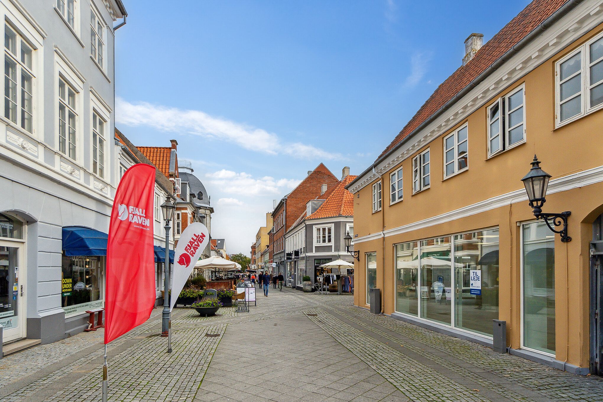 Butiksgade med røde flag og røde tagdækninger og flere butikker og gafler samt folk, der går