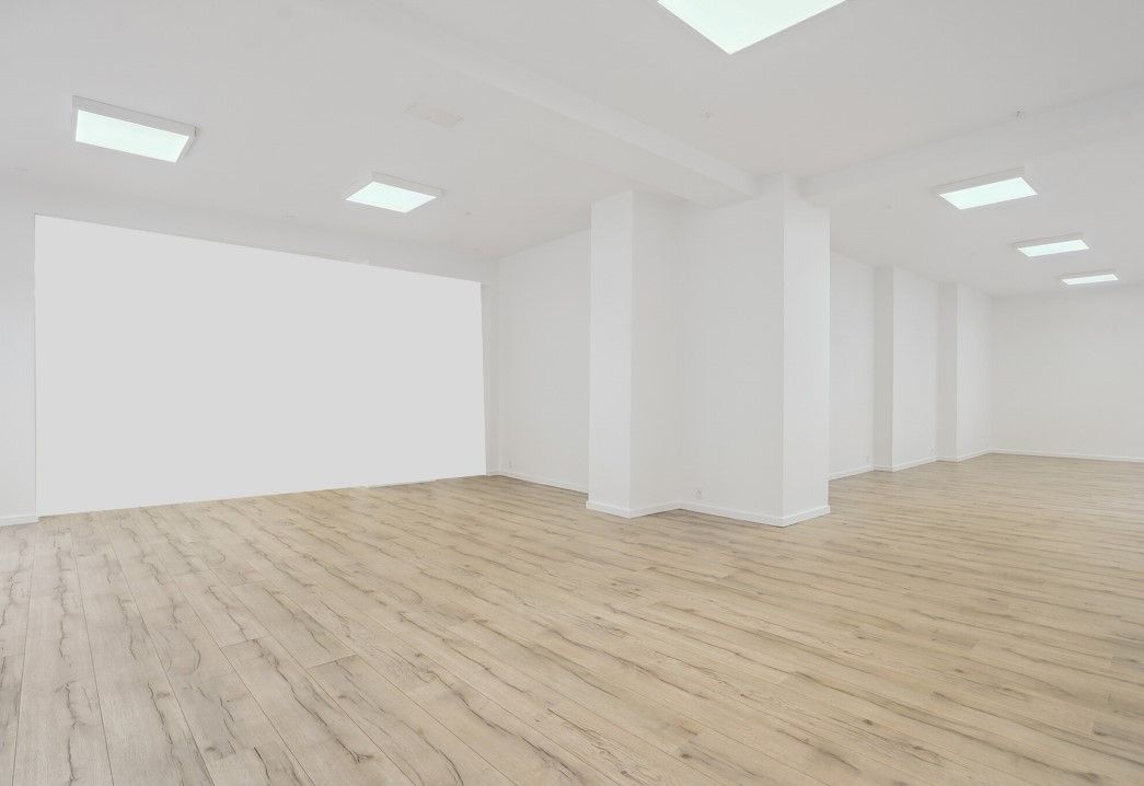 En stor, lys, tom butikslokal i Nyborg med lysegul gulvbelægning og hvide vægge samt hvide loftsbærere og indlejrede