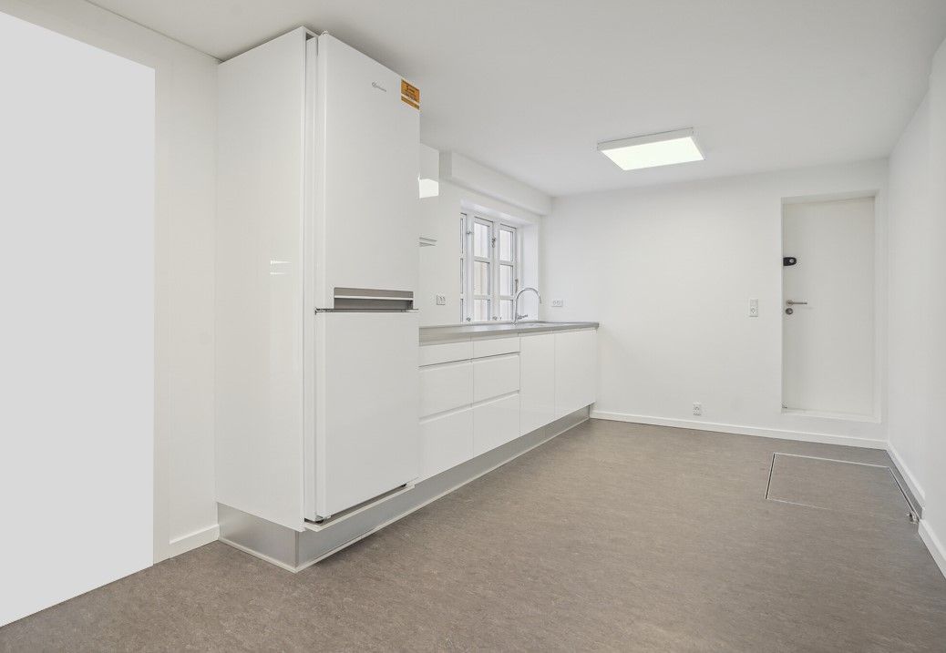 Moderne og minimalistisk køkken med hvide vægge og loft, hvidt køleskab, rustfrit stål komfur, hvide skabsfronter, indbygget