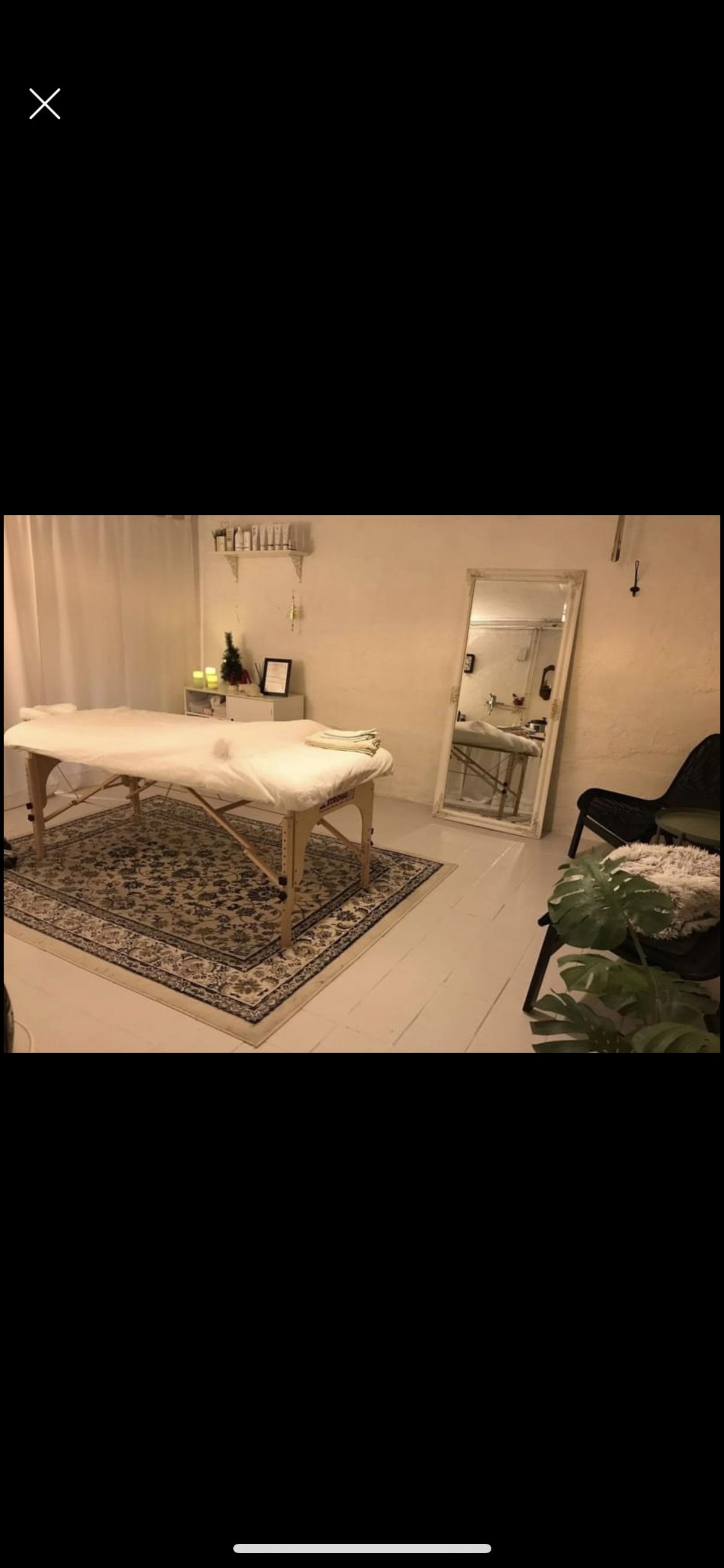 Spa-område med massagebord og tæppe, spejl og plante samt møbler og dekorationer på væggen