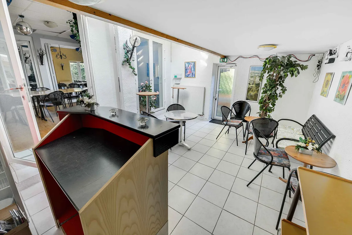 En stor, lukket café med lyse interiør, runde borde, lysegule vægge og en stor plante i hjørnet