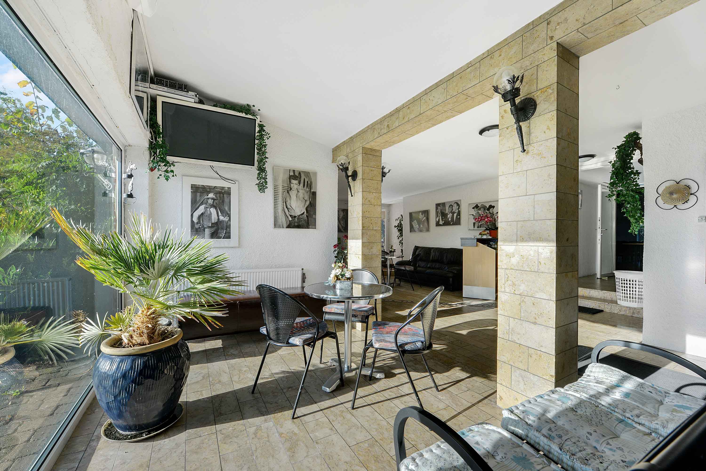 En hyggeligt indrettet veranda med bord, stole og puder, tv på væggen og plante i gryde