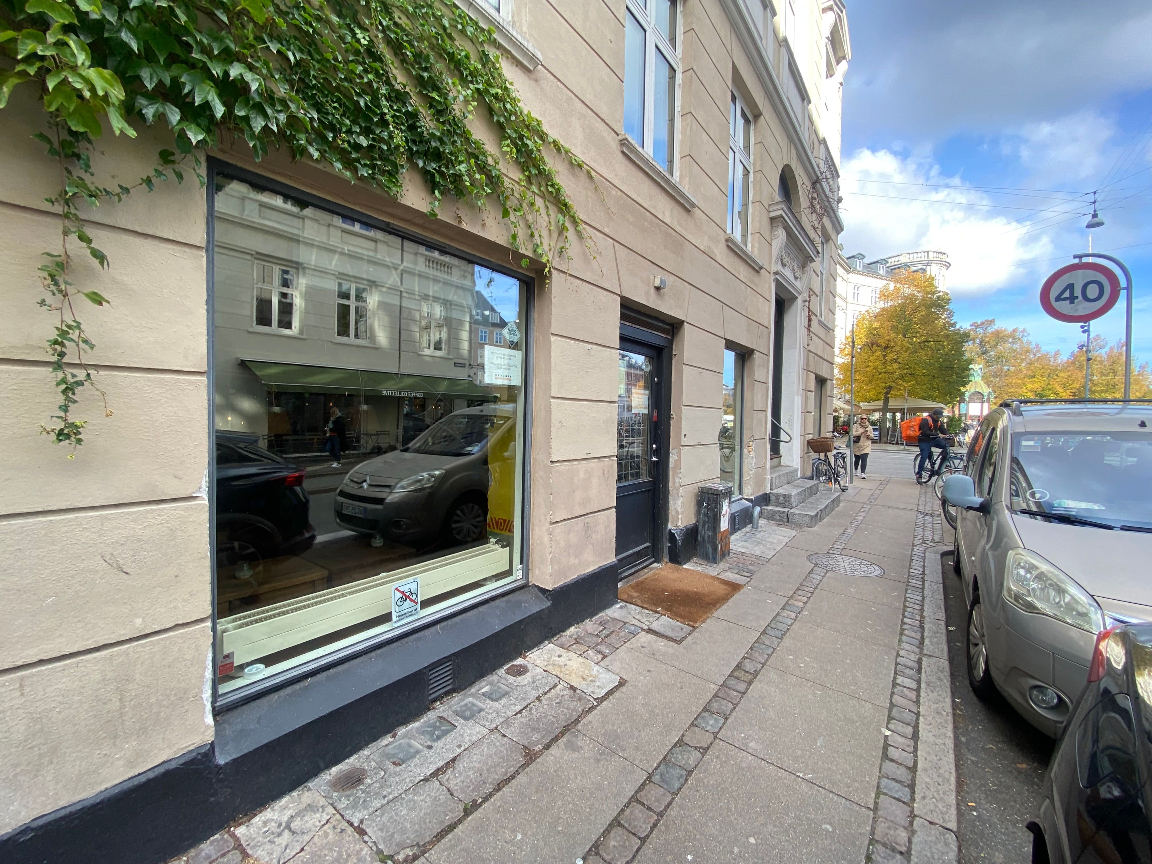 Et glasfrontet forretningslokale med plantevækst på facaden og et skilt med 40 km/t i baggrunden