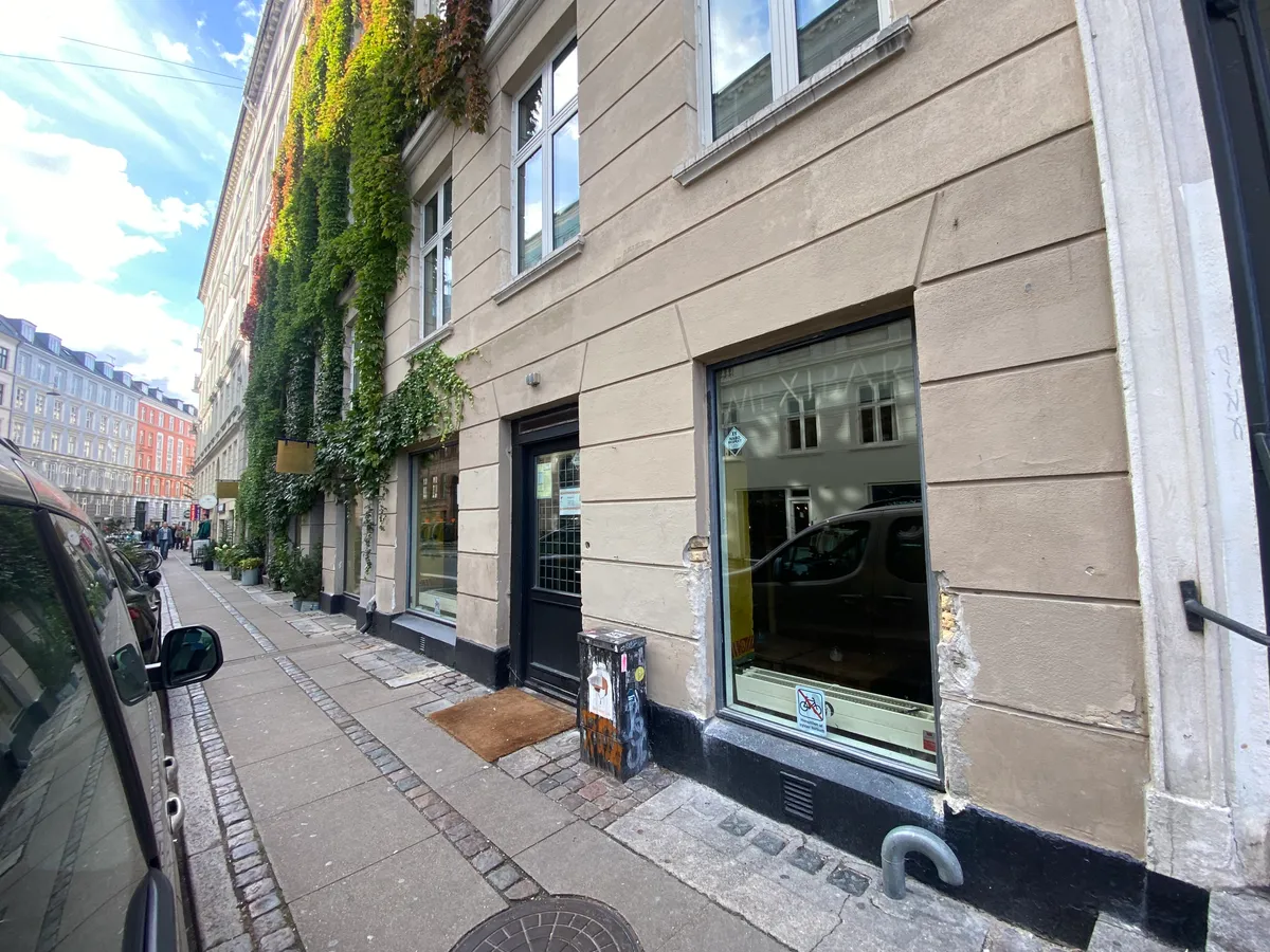 En stor bygning med grønne planter og en høj skorsten står på en gade med en bilparkeret bil og en tyk skorsten