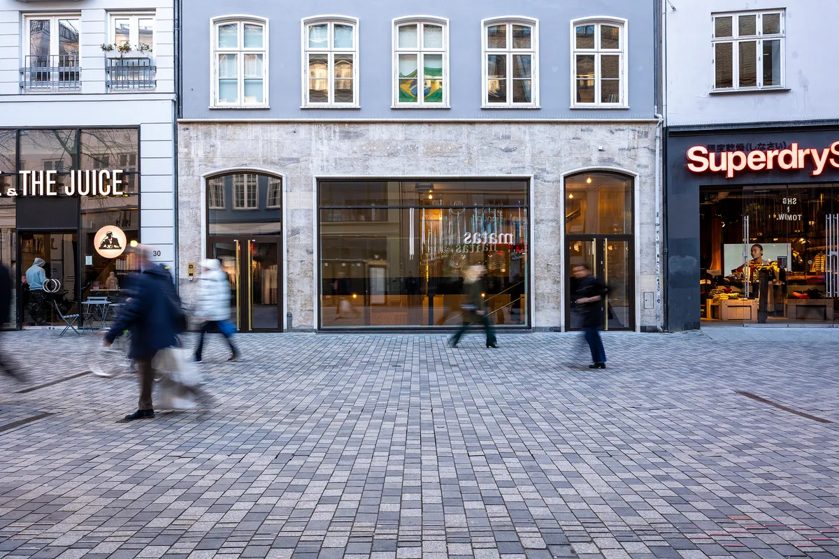 Mennesker går forbi Superdry og The Juice, der er butikker i baggrunden, og der er flere mennesker i midten. Butikkerne