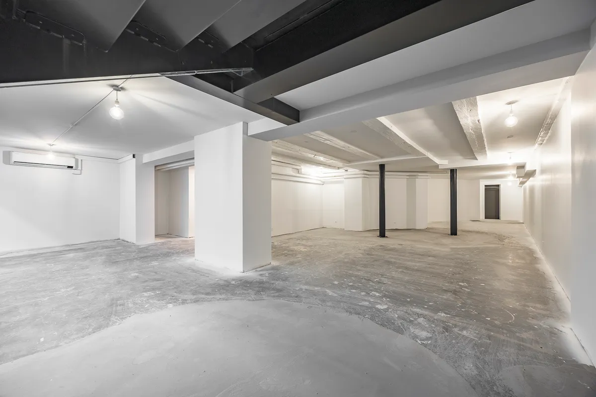 Store tomt rum med cementgulve, flere hvide vægge, og lysekroner. Loftet er højt og er i sort. Der er et klimaanlæg monteret
