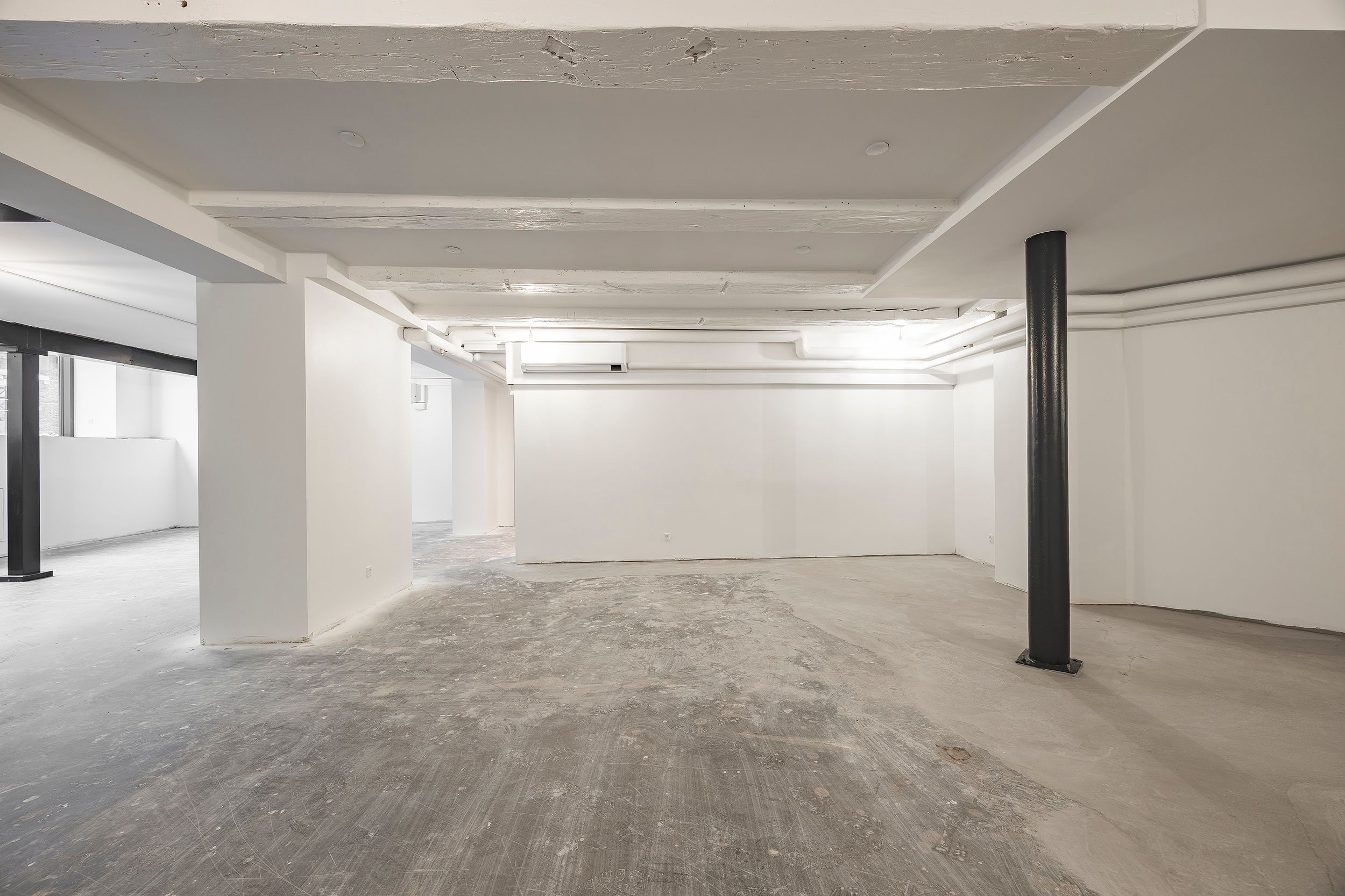 En stor, lys, industriel indretning med højt loft, hvid gulv og vægge samt to høje, sorte støtter i midten af rummet