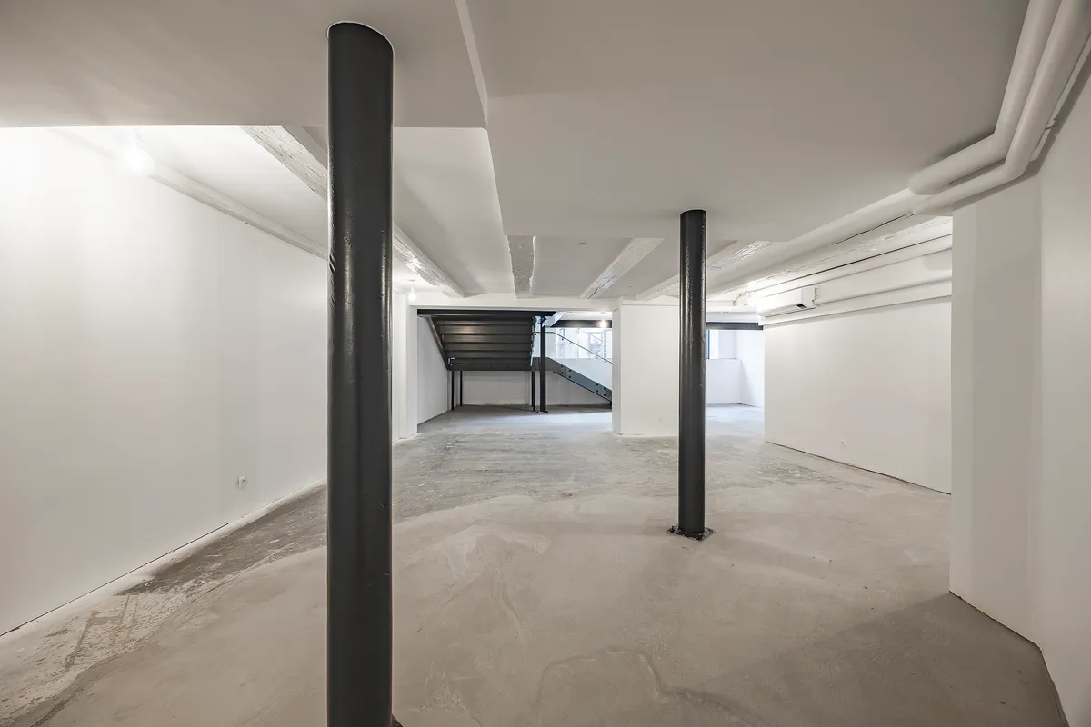 En ubenyttet lagerlokale med hvide vægge og højt til loftet med lysekroner og en trappe i midten