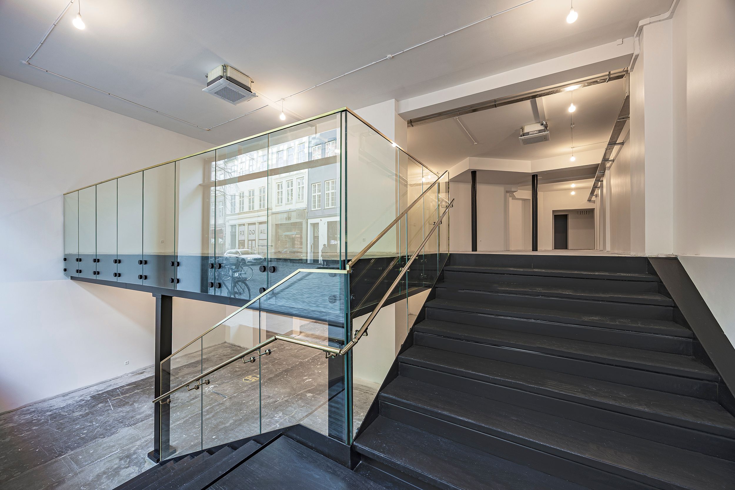 Glasdækket trappe med slanke guldfarvede håndtag og glasvægge leder op til den øverste etage af en moderniseret bygning.