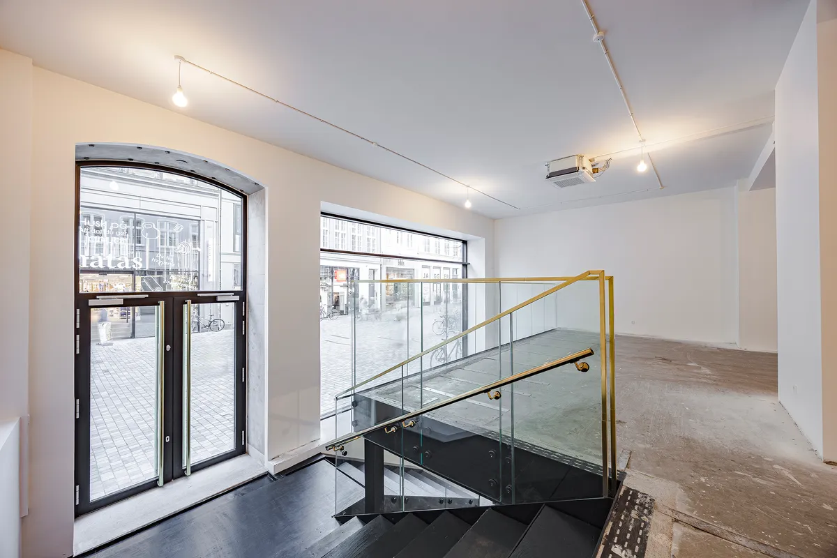 Ny stueetage med vinduesfront og trappe til 1. sal, udsmykket med lysekroner og glas. Glasdøre og vinduer med udsigt til