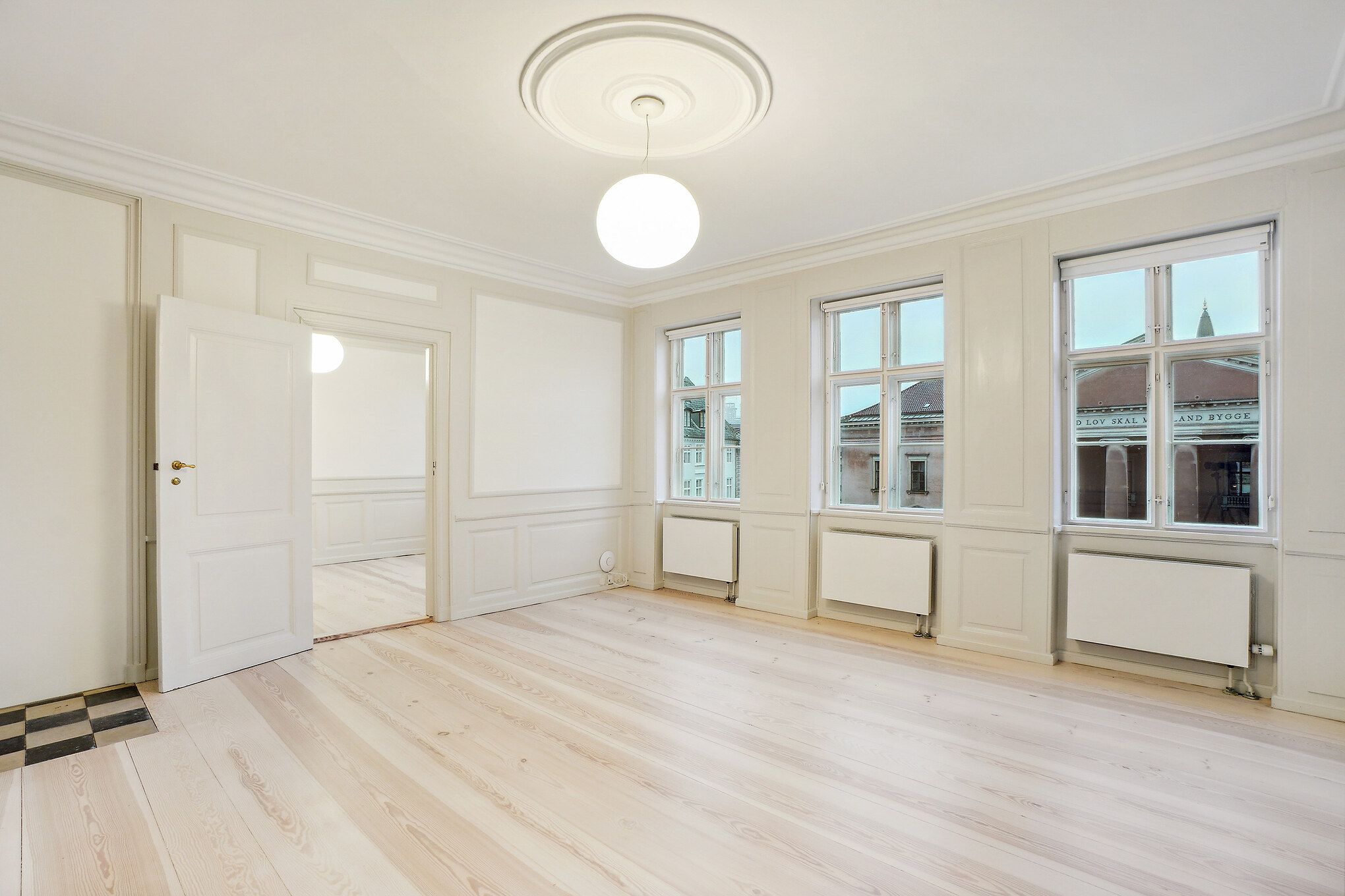 Lyst og rummeligt værelse med hvidt loft, gulv og vægge. To store vinduer med udsigt til Nytorv og Københavns Byret. Elegant