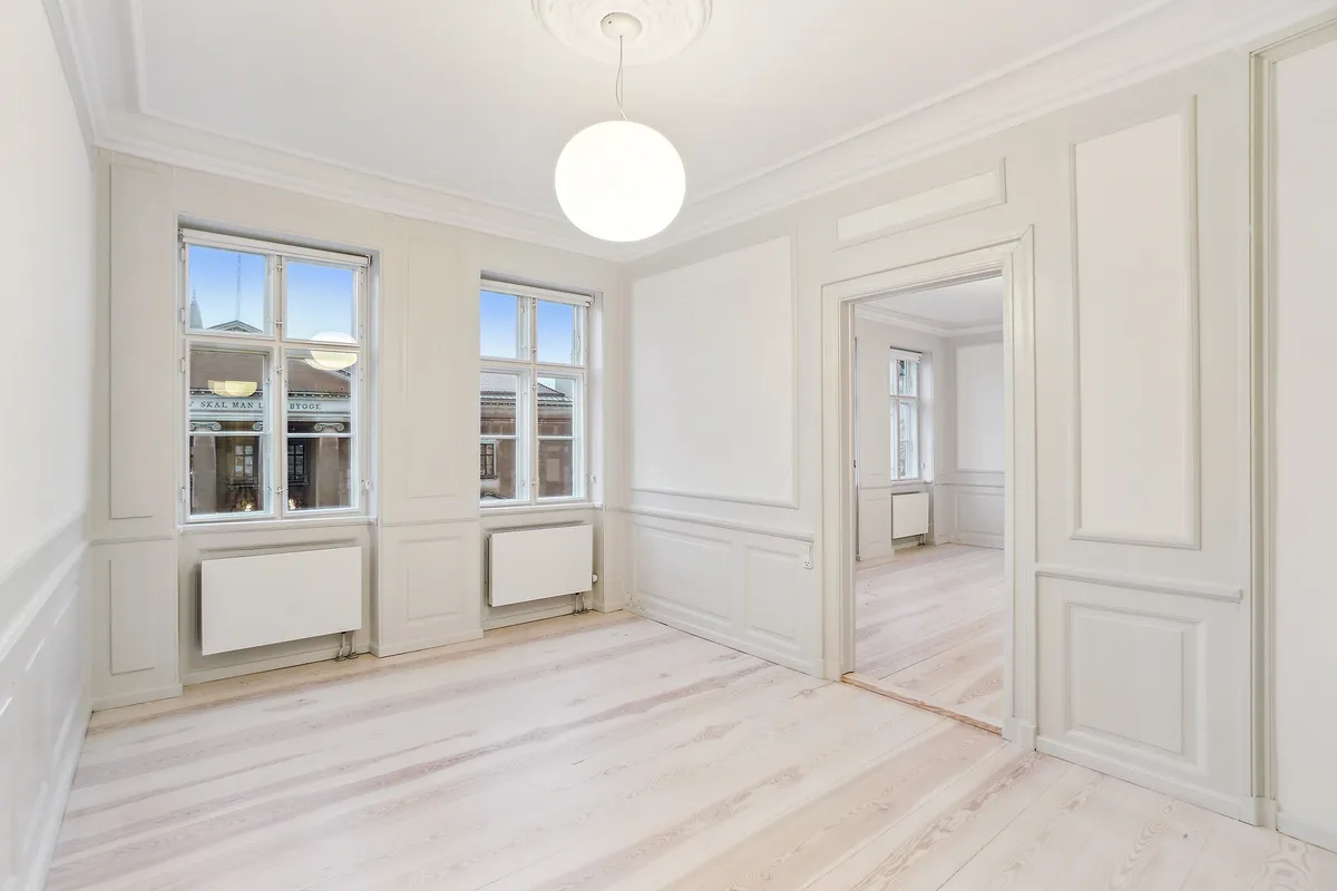 Et pænt værelse med hvide vægge og lyse trægulve samt to store vinduer med udsigt over Københavns Byret og Nytorv