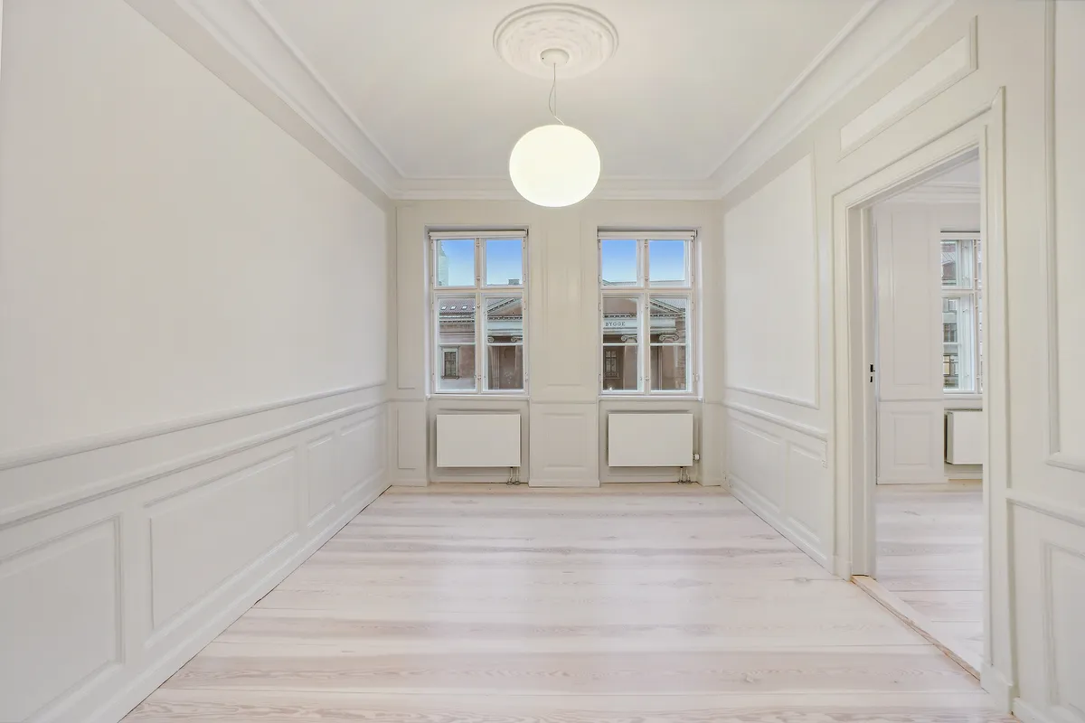 En stor og lyse hall med lysegult trægulv, to store vinduer og et rundt loftslys