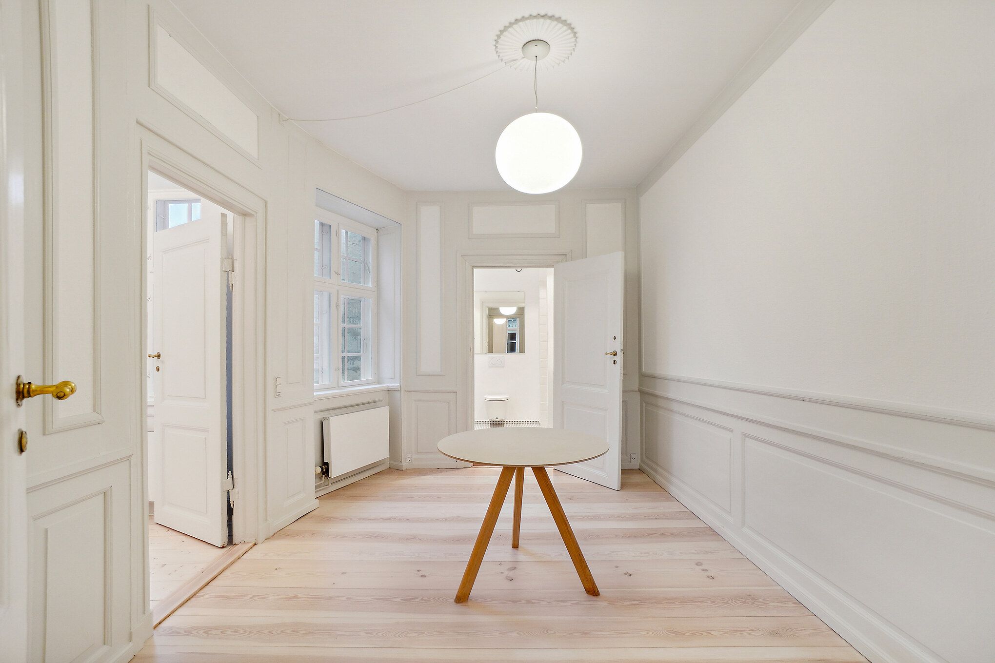 Elegant og velplejet interiør med hvidt panel og lysegult gulv. Et rundt hvidt bord med træben og en hvid lampestolpe. To