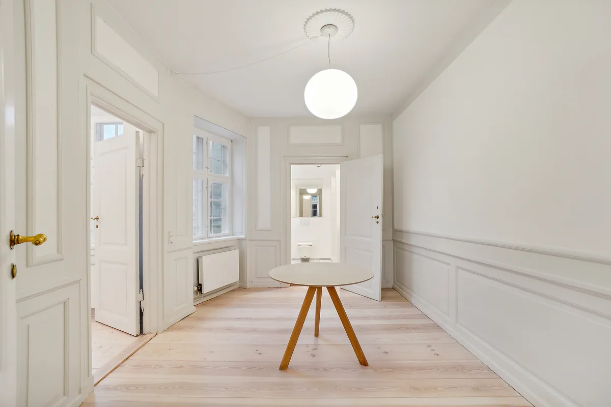 Elegant og velplejet interiør med hvidt panel og lysegult gulv. Et rundt hvidt bord med træben og en hvid lampestolpe. To