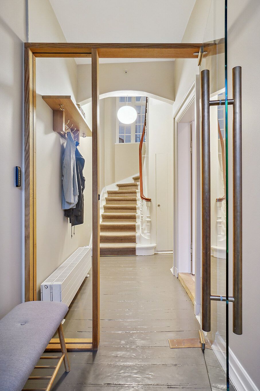 Glassdør og træramme med garderobe og trappe op til første sal med lyse og højloftede rum