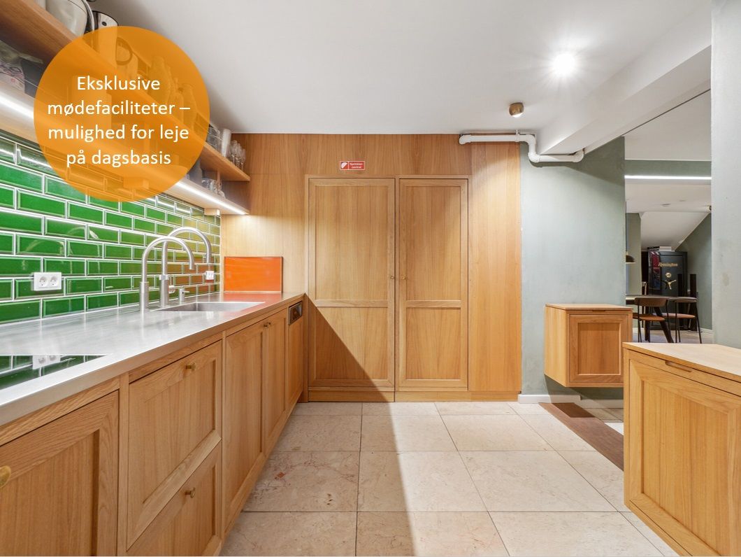 Moderne køkken med lysegrå og grønne teglstensvægge, højloft, lysekroner, lyseskabe, køkkenhylder, træskabe, spisestuebord,