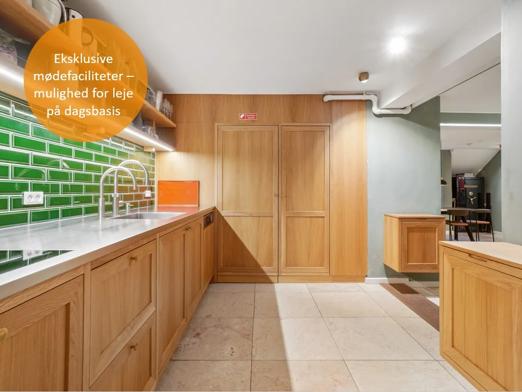 Moderne køkken med lysegrå og grønne teglstensvægge, højloft, lysekroner, lyseskabe, køkkenhylder, træskabe, spisestuebord,