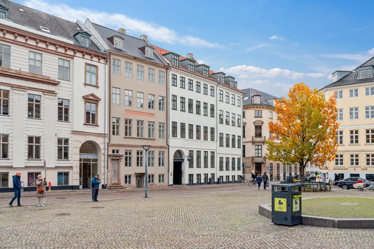 Mennesker går på Nytorv med udsigt over Københavns Byret og en stor træ i centrum. Man ser en skulptur og en skraldespand