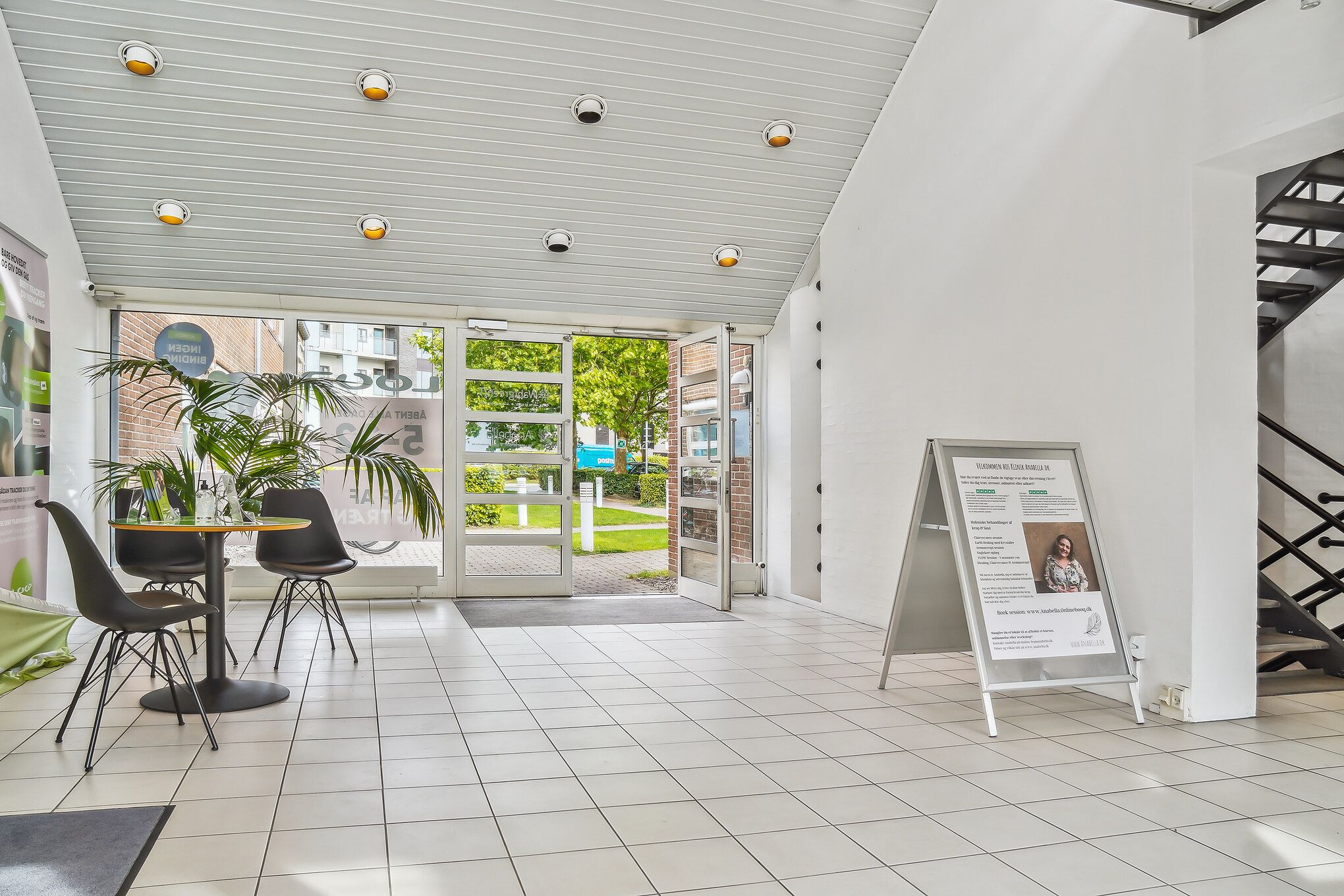 Indvends er der en indgangsdør, der fører ud til en grøn park. Værelset er lyse og ren med en bord og stole og en plakat med