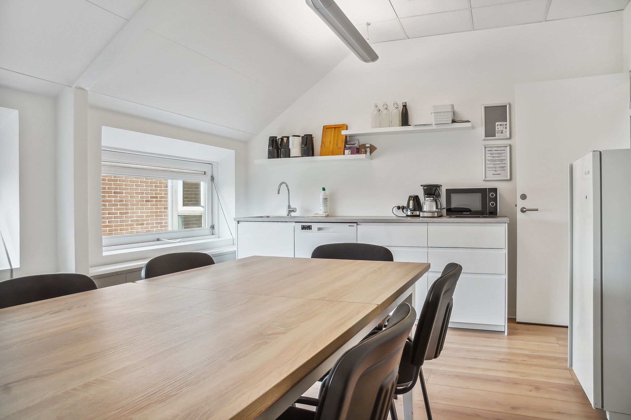 Moderne køkken med lys, lyseblå loft, hvide vægge og trægulv samt et bord med stole og køleskab