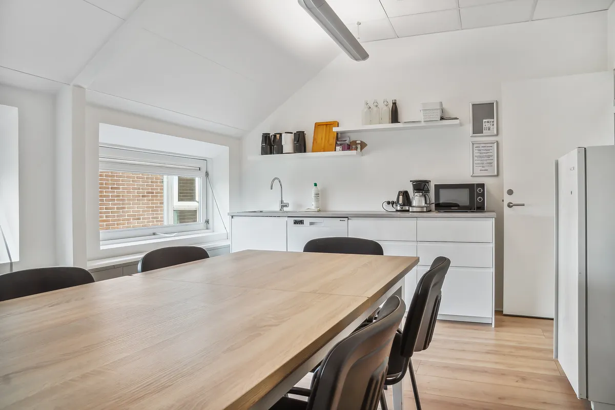 Moderne køkken med lys, lyseblå loft, hvide vægge og trægulv samt et bord med stole og køleskab