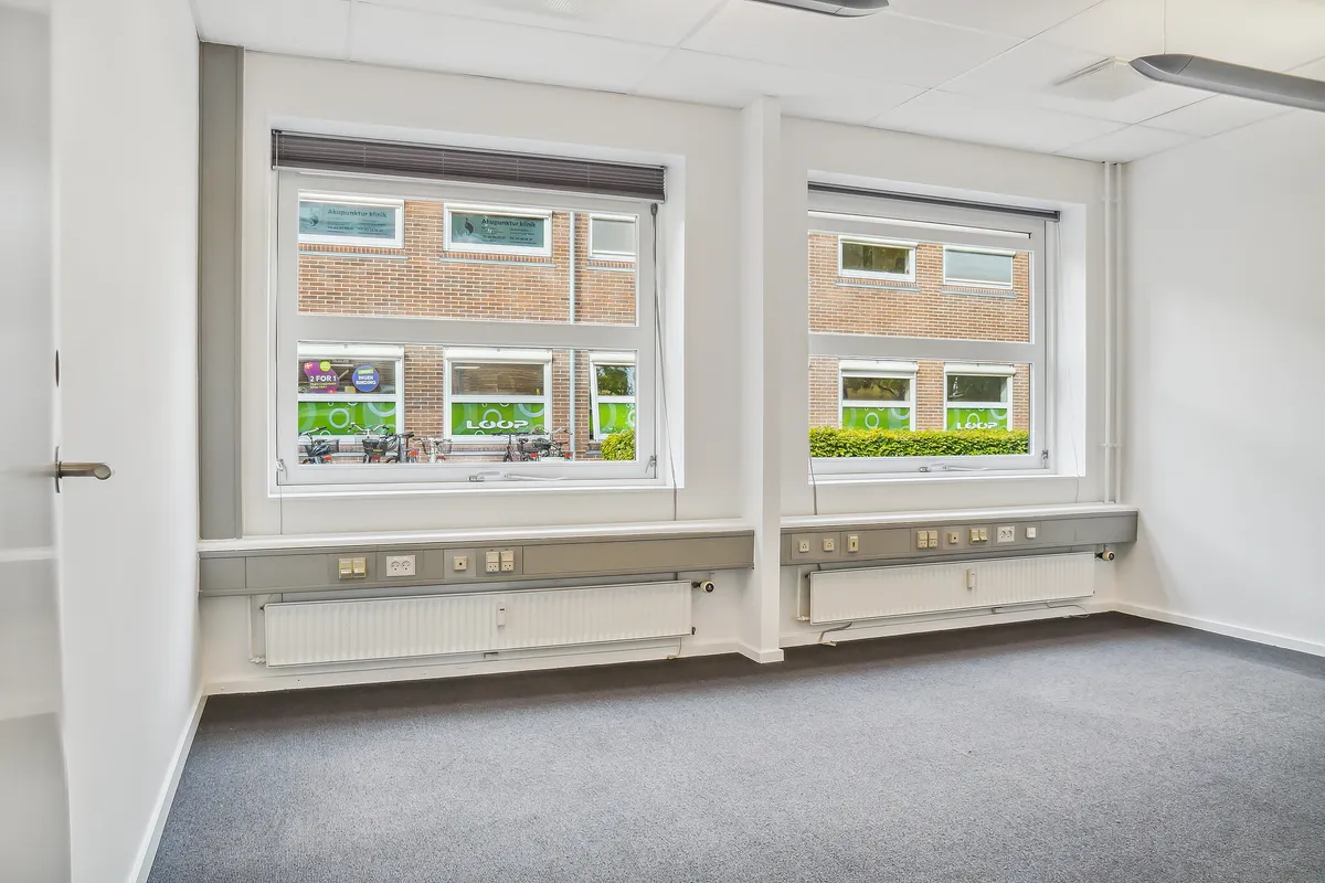 En lukket dør med håndtag og to store vinduer med grønne skilte og en række radiatorer under hver vindue