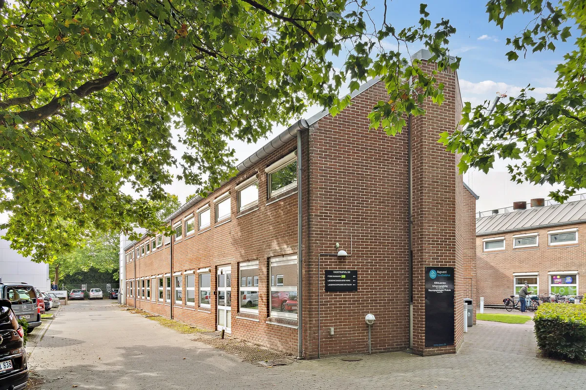 Tegn for Baggårdstuen og Baggårdsfællesskabet er synlige på en mur. Der er en søjle med et rundt lys og en affaldskur på