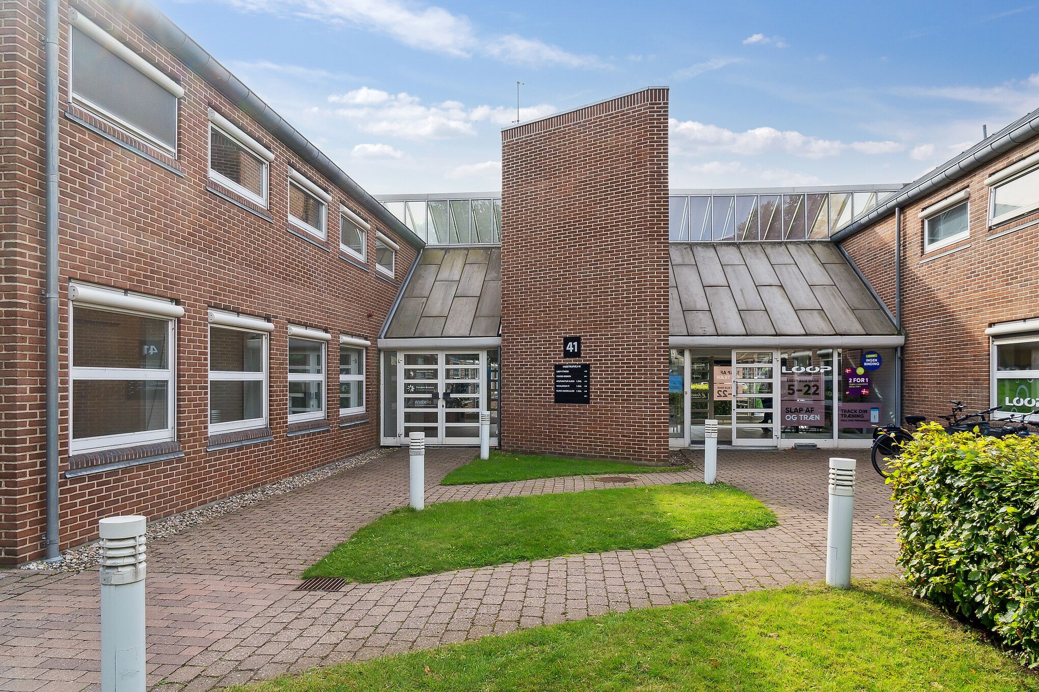 Lokaler i klinikfællesskab med enkeltindgang og nummerplade 41. Her er slette græsplæner, bollarder og to parkerede cykler.
