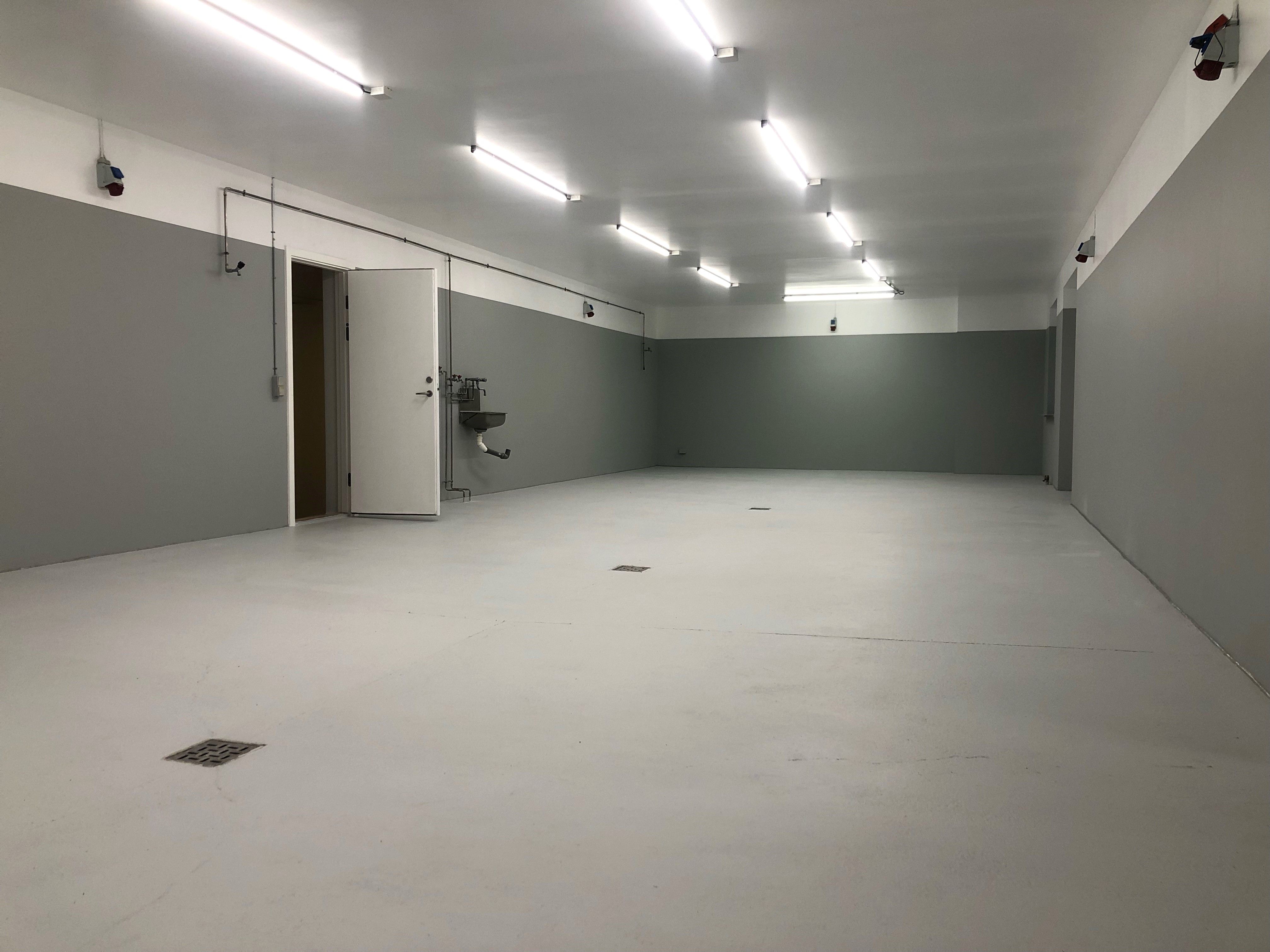 En ren og tom lagerhal med hvide vægge og gulv samt lysekroner i loftet og en åben dør