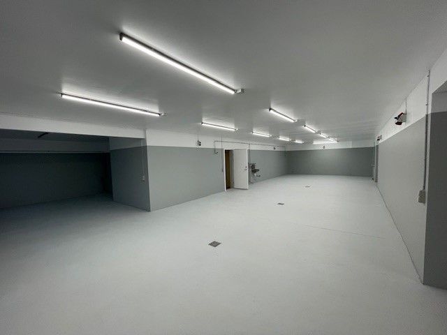 Et stort, tomt og lyse hængeloft med hvide lysekroppe, en lysegul væg og en dør.