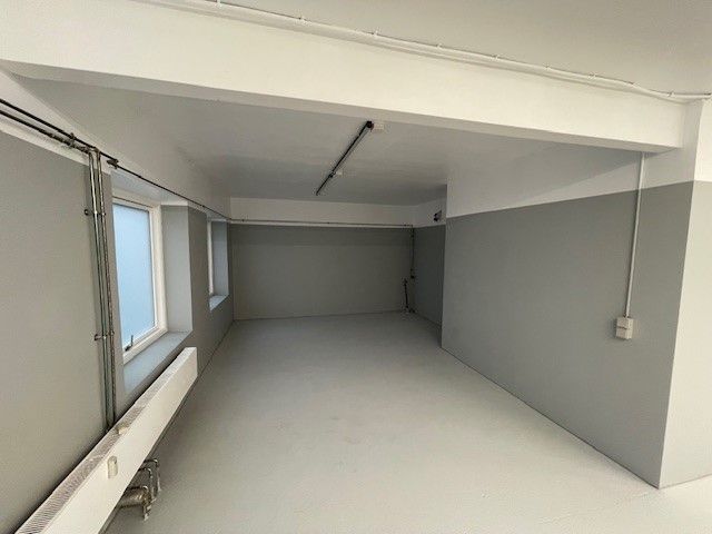 En tom lagerhal med hvide og grå vægge, to små vinduer og en gulvvarme langs den ene væg