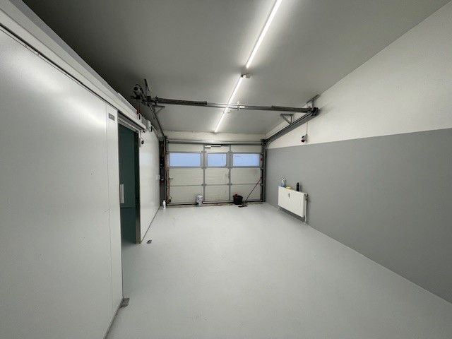Regelmæssigt garagelokale med åbne garageporte og store vinduer, lyse hvide vægge, gulv og loft og to udgange til siderne