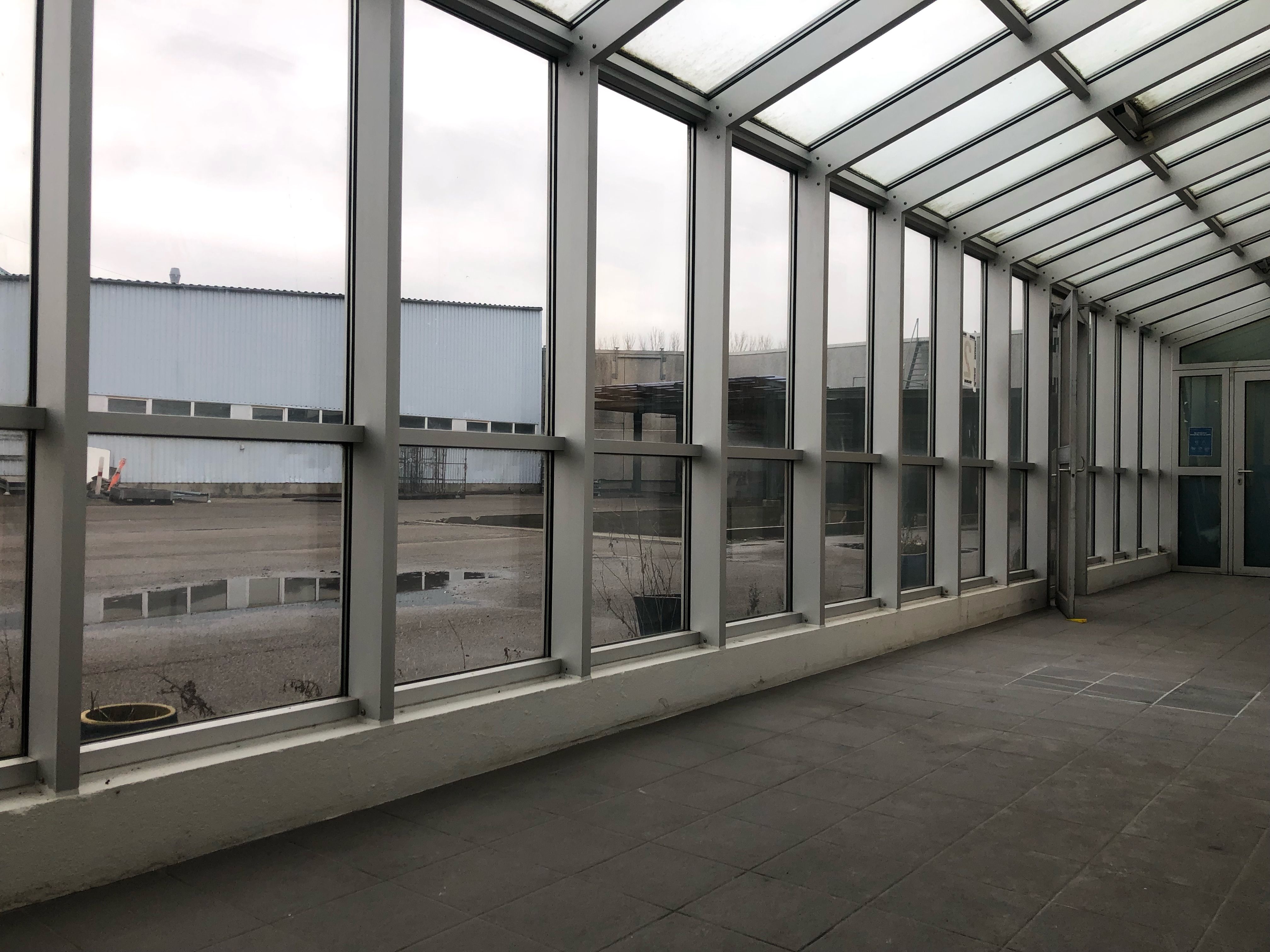 Store, glaspaneler med rammer i lysegråt. Betongulv med mønstret udformning. Lysegrå metalkonstruktioner og tætte, hvide