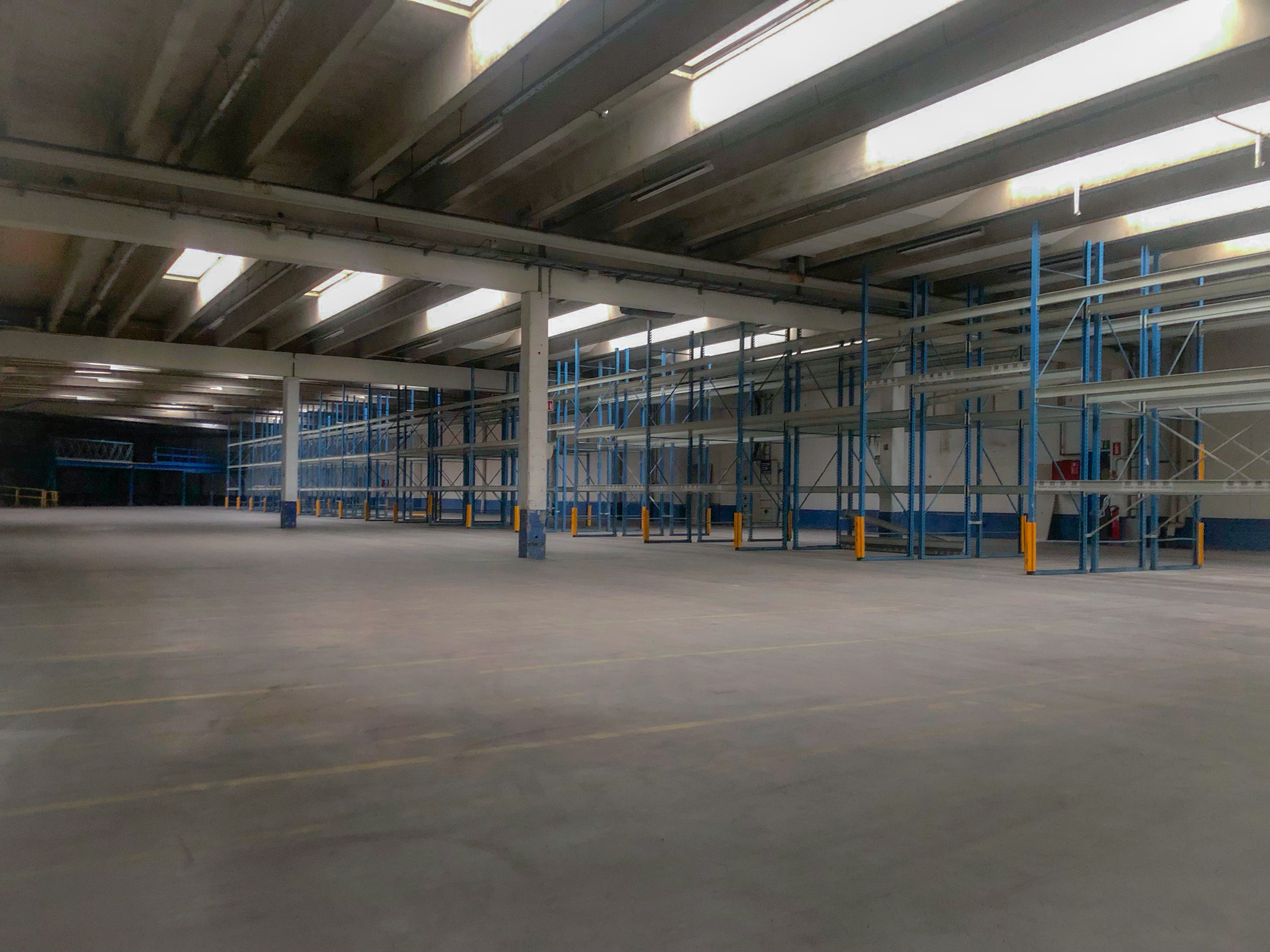 Lagerlejemål med højloft og højt lys, rækker af lagerhylder, gulve med gul linjemarkering og gule poller for at markere