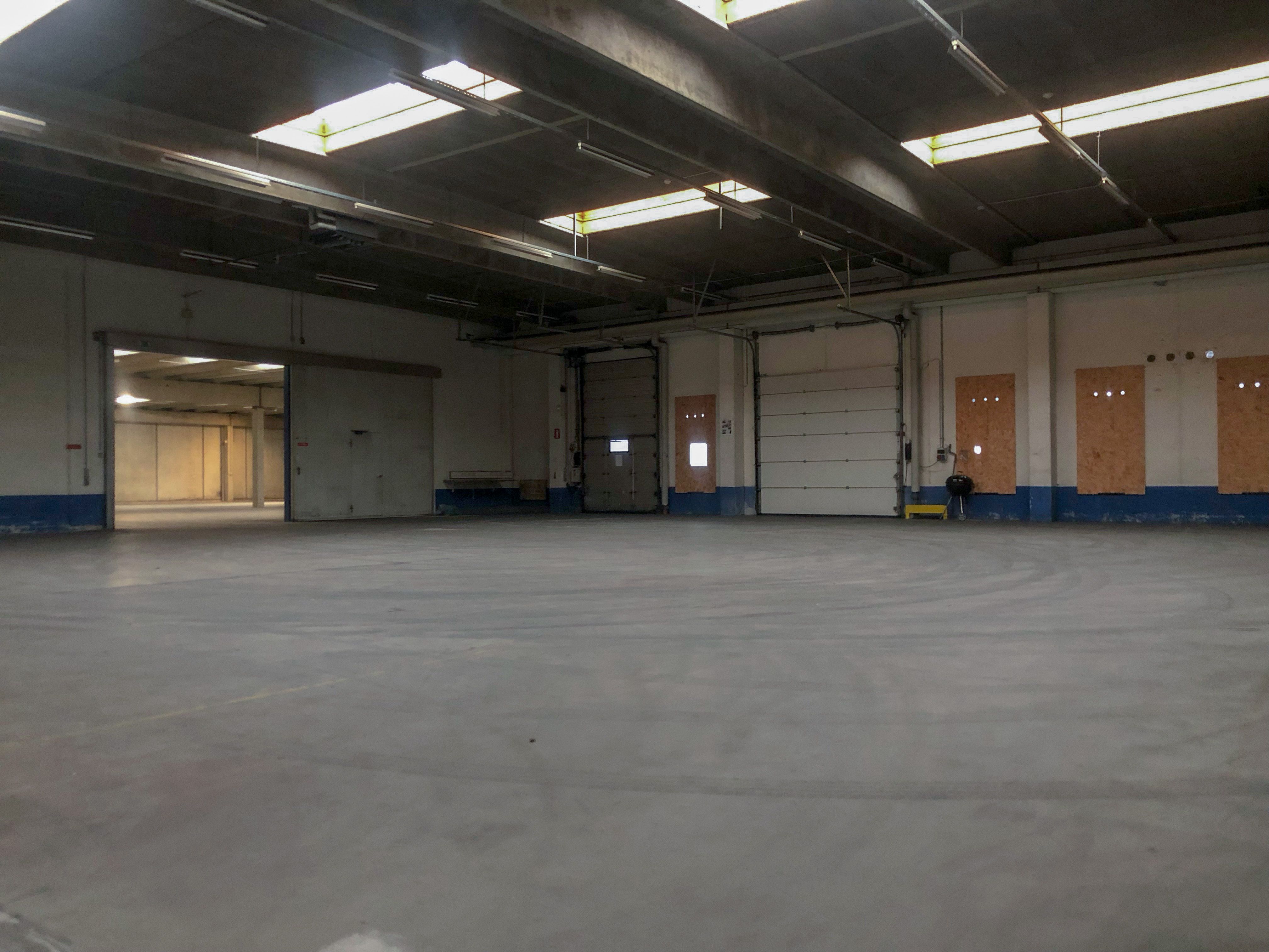 Et stort, tomt lager med hvide vægge og en høj loftshøjde, samt store garagedøre og vinduer i loftet