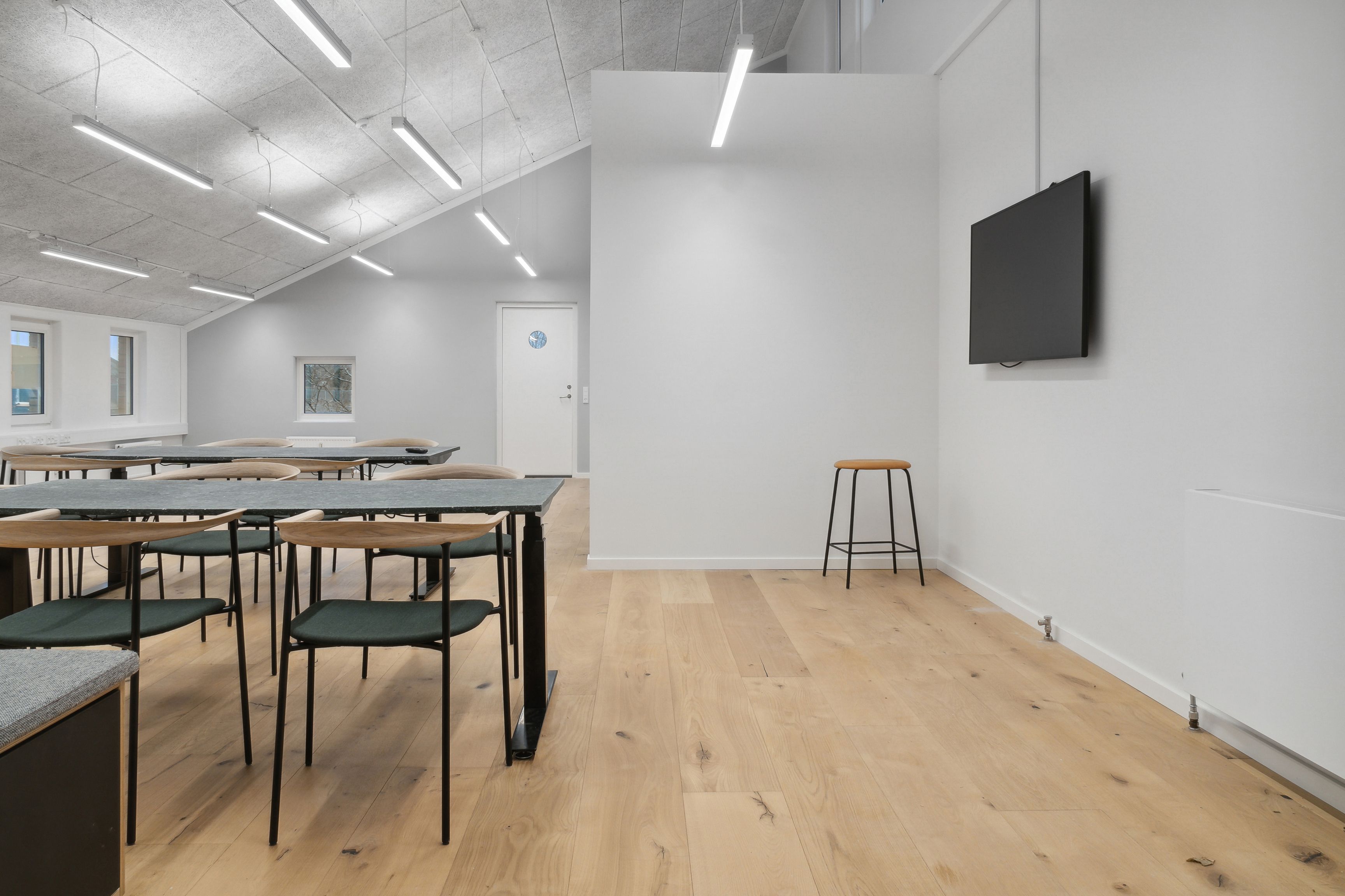 Et tomt lokale med højt loft, lyse paneler, møbler og en fjernsynsskærm