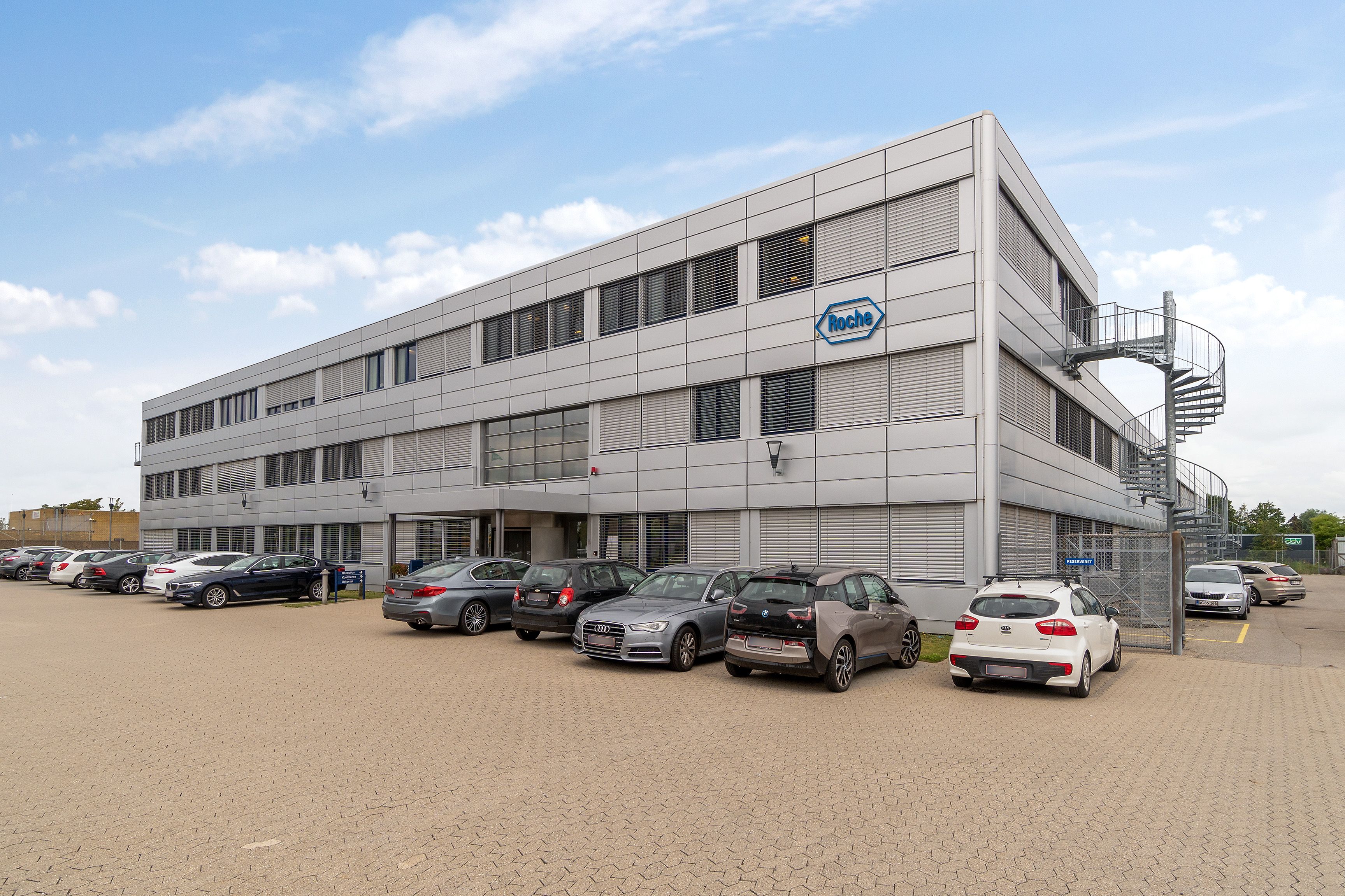 Firmabygning med parkeringsplads for biler med et skur, en spiraltrappe og en tydelig logopåskrift Roche