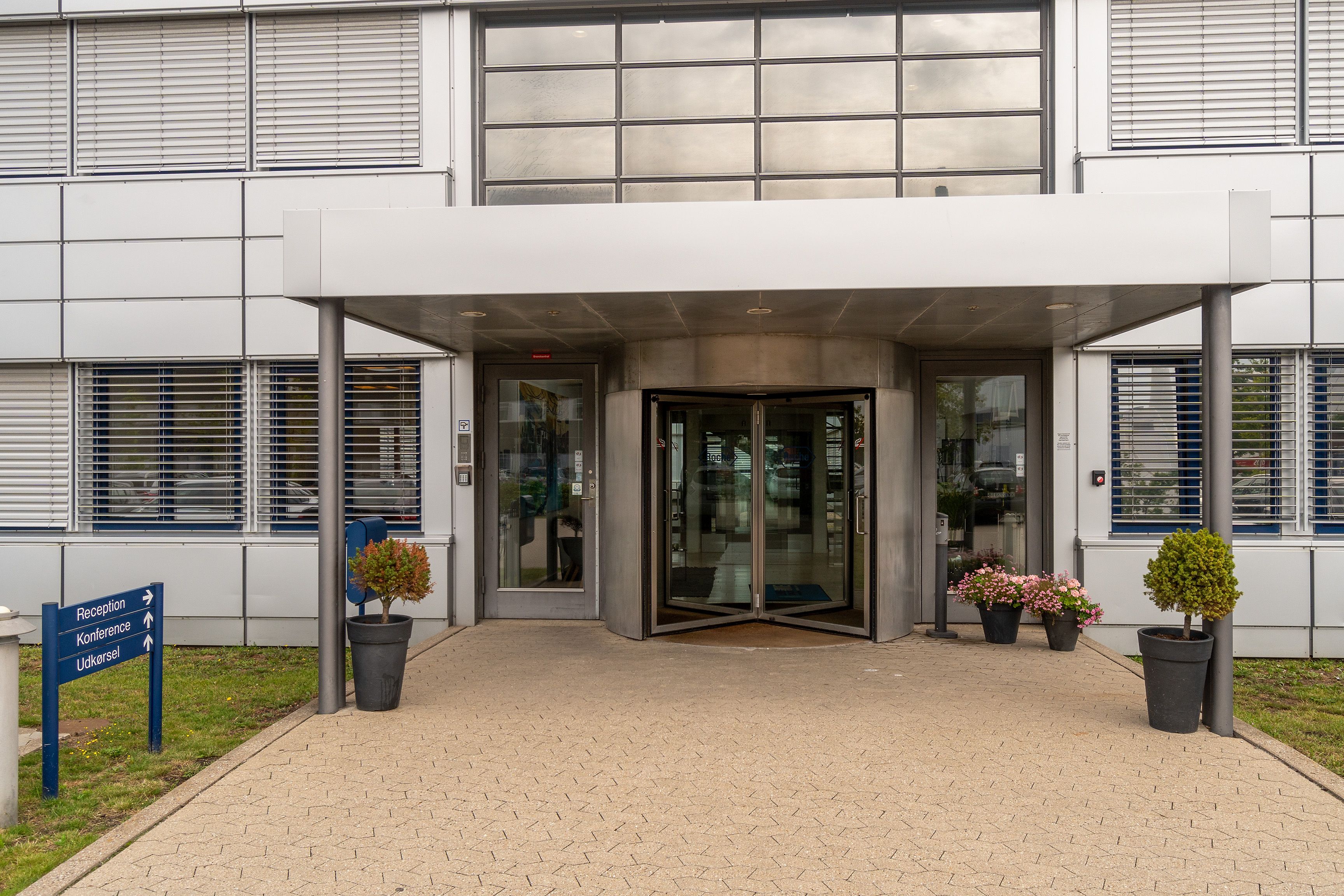 Moderne bygning med hvide vægge, automatiske glasdøre, kantede bordplader og 4 lyserøde og hvide blomster i potter foran
