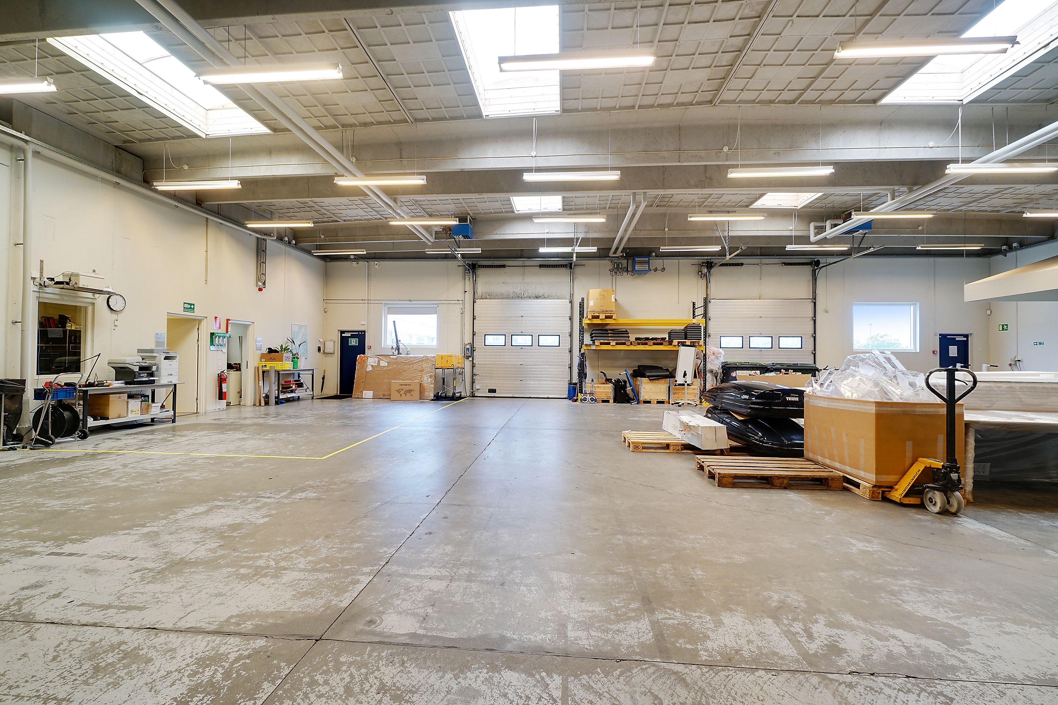 Stort lejemål med mange muligheder. Her er højloftede lokaler med lyse loftsvinduer og store garageporte.