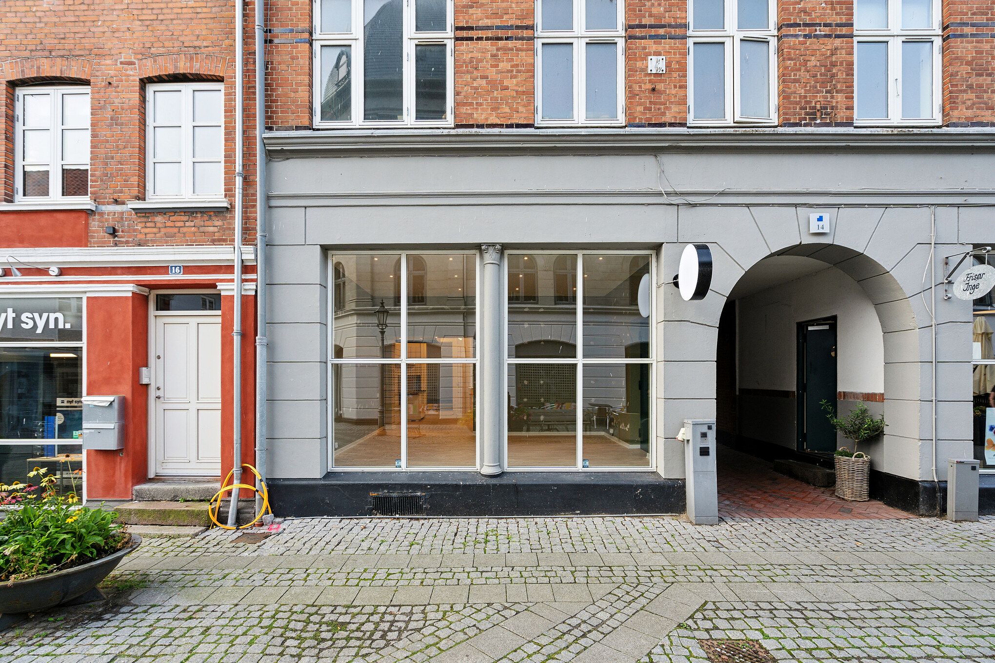 Butikslokale i Nyborg med glasruder og trægulv, lysekroner og en plante i kurv, foran ligger gulvtæppe