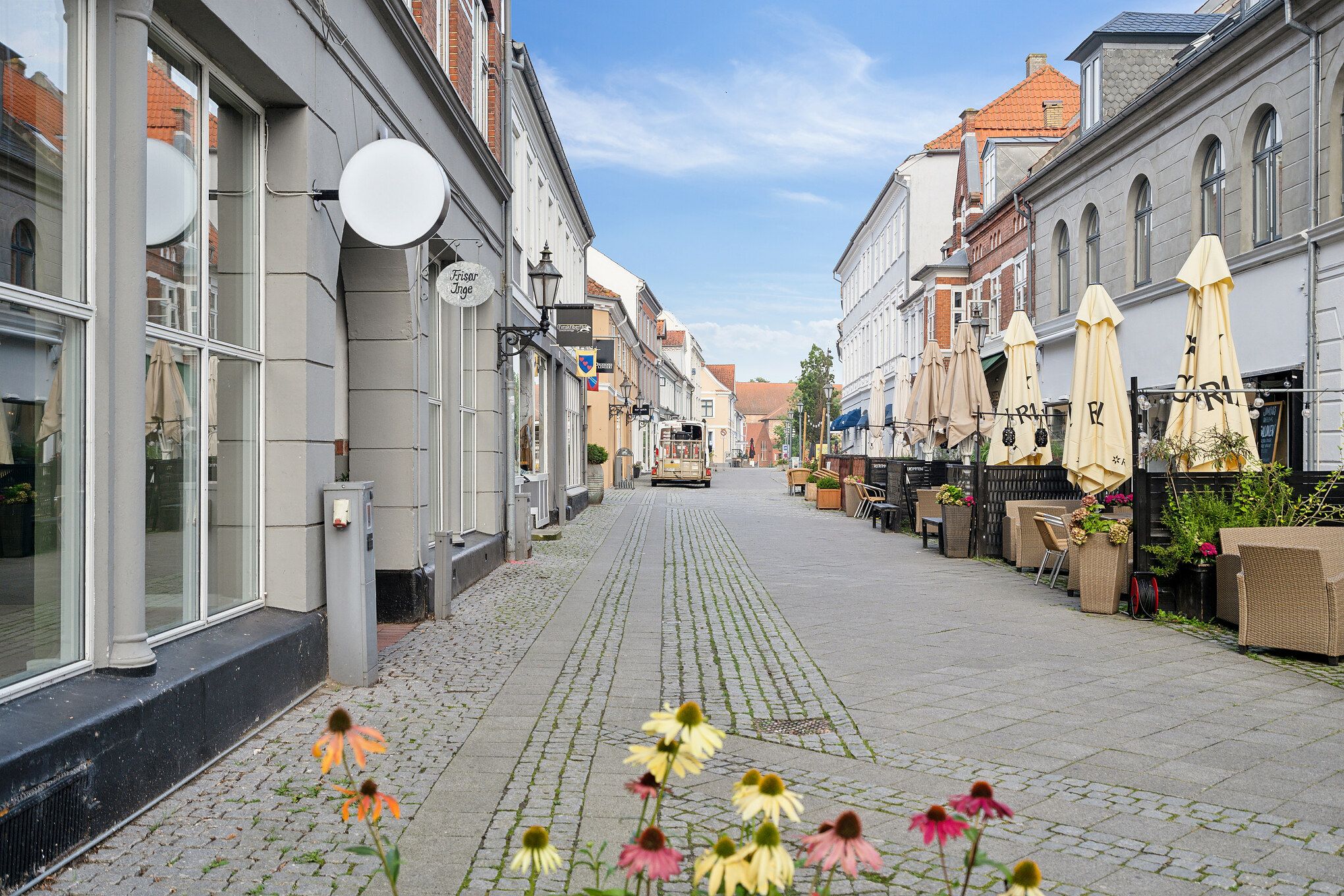 Gågade med butikker, blomster, parasoller og plantepoter langs med den.