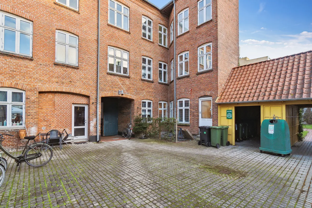 En tom gågade med røde murstensbygninger og trækummer. Et snavset spildevandscenter og to spildevogne. En cykelparkeret ved