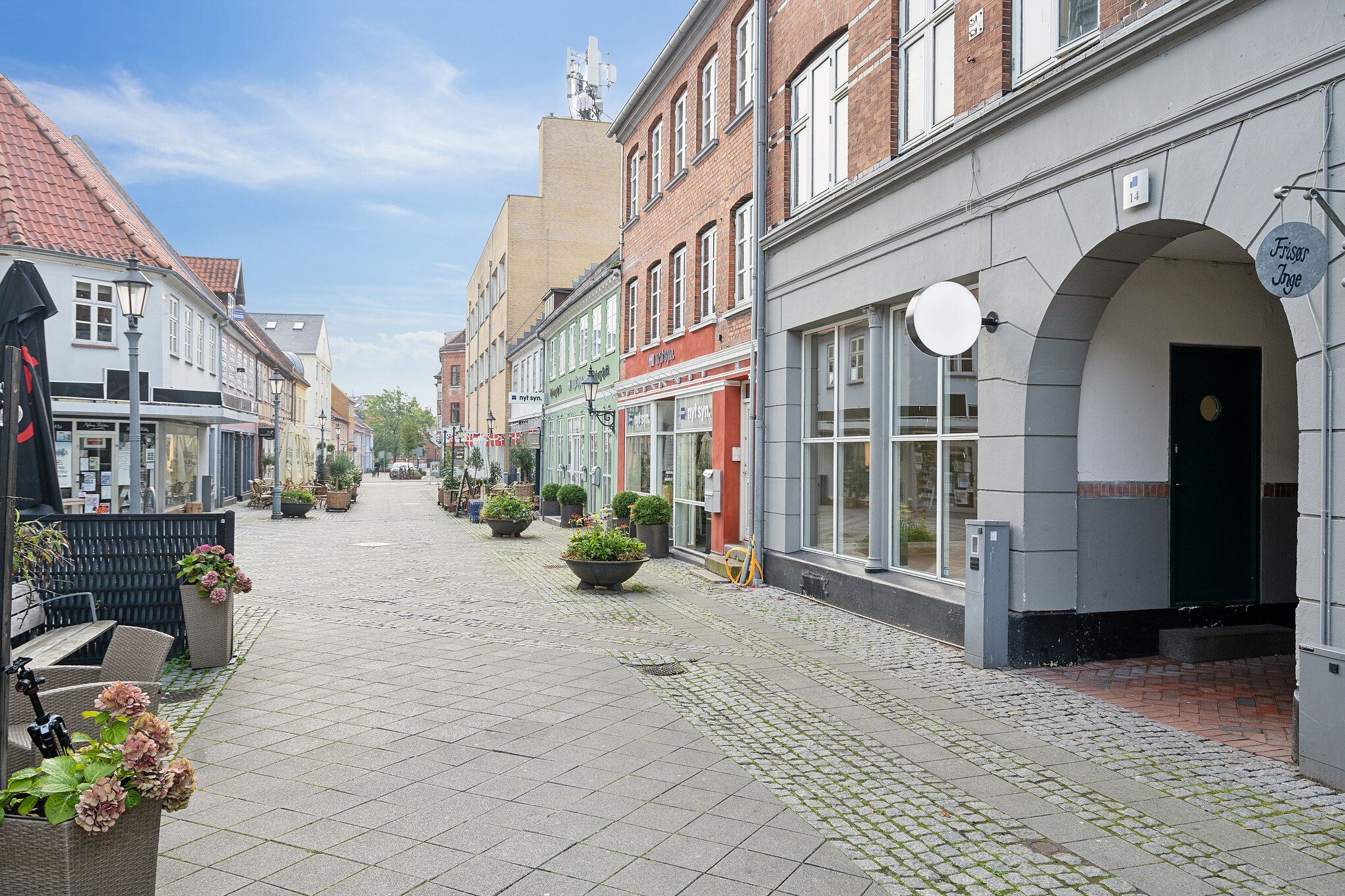 Nyborgs gågade med forretninger og grønne potter med blomster i centrum og lyse himmel på baggrunden