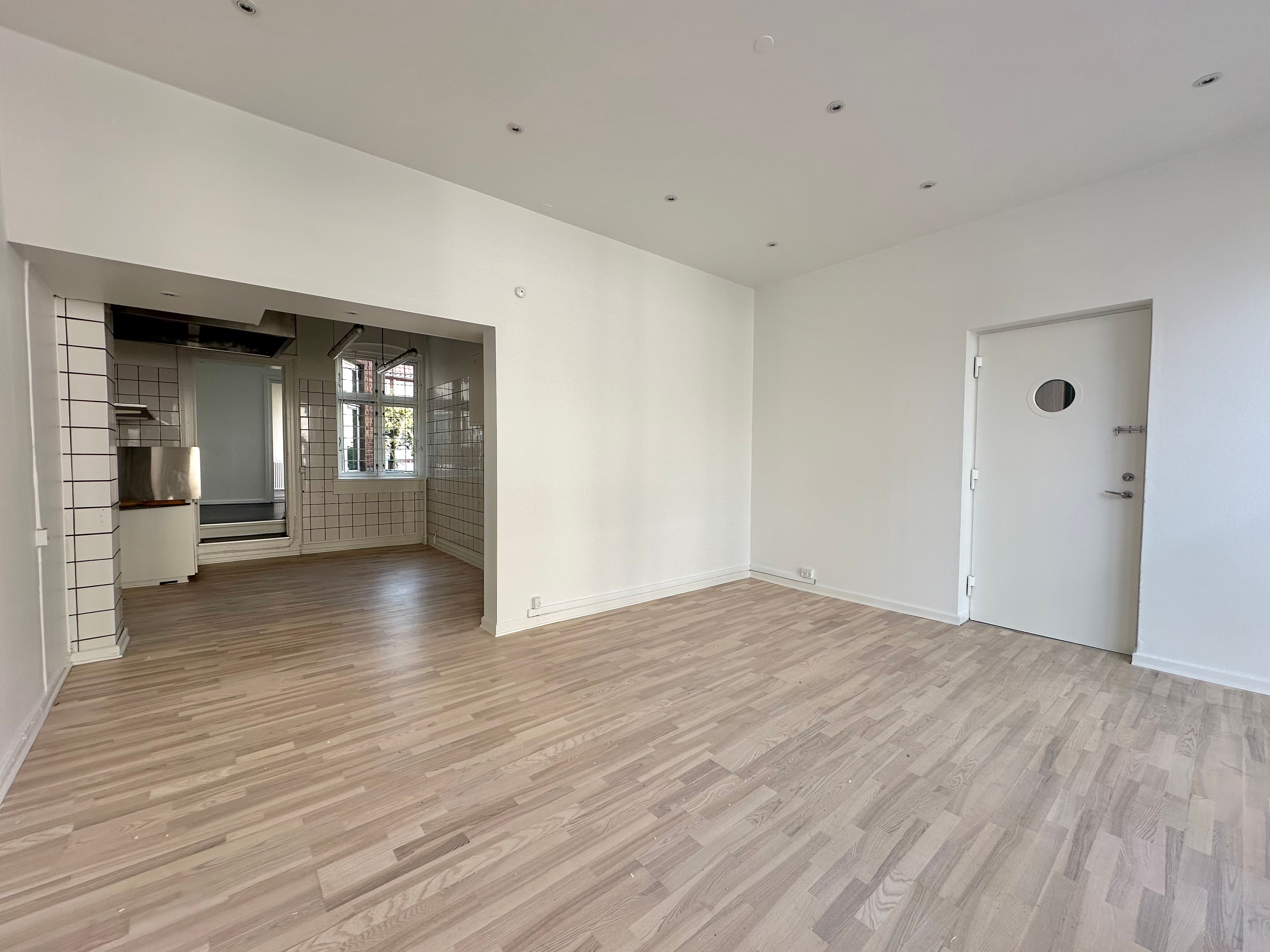 En stor tom rum med hvide vægge og lyse trægulve og en dør med rundt udskæring i døren