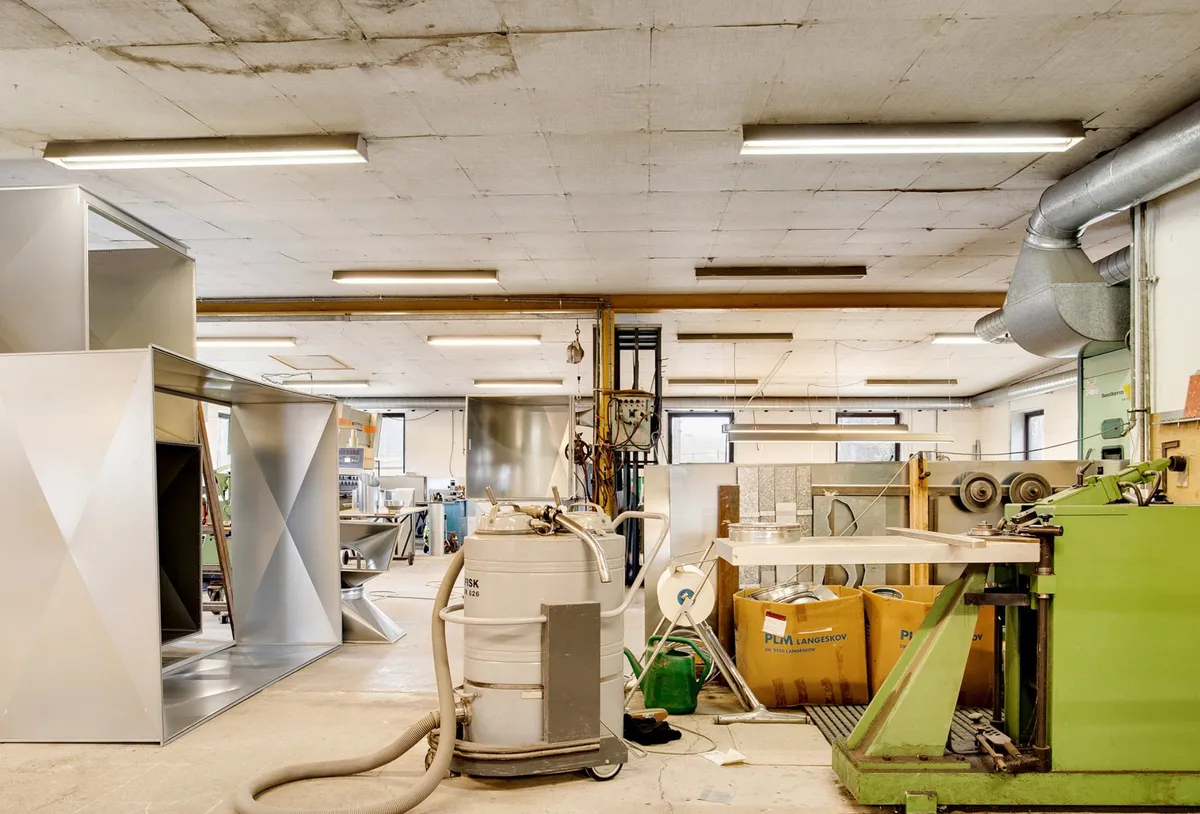 Industriområde med flere maskiner og værktøj samt lagerkasser og en støvsugemaskine i midten af rummet