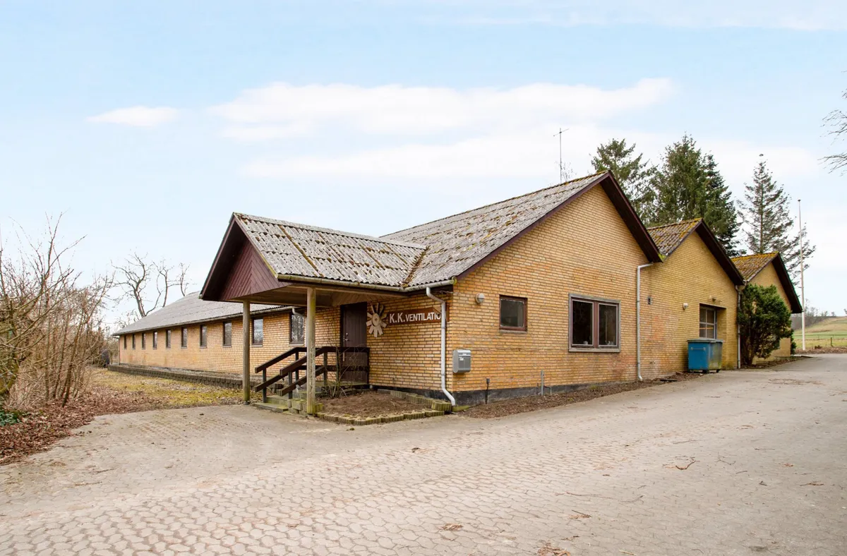 En gammel murstensbygning med skilt, K.K. Ventilation, og skrånende tag med en stor skur og skraldcontainer