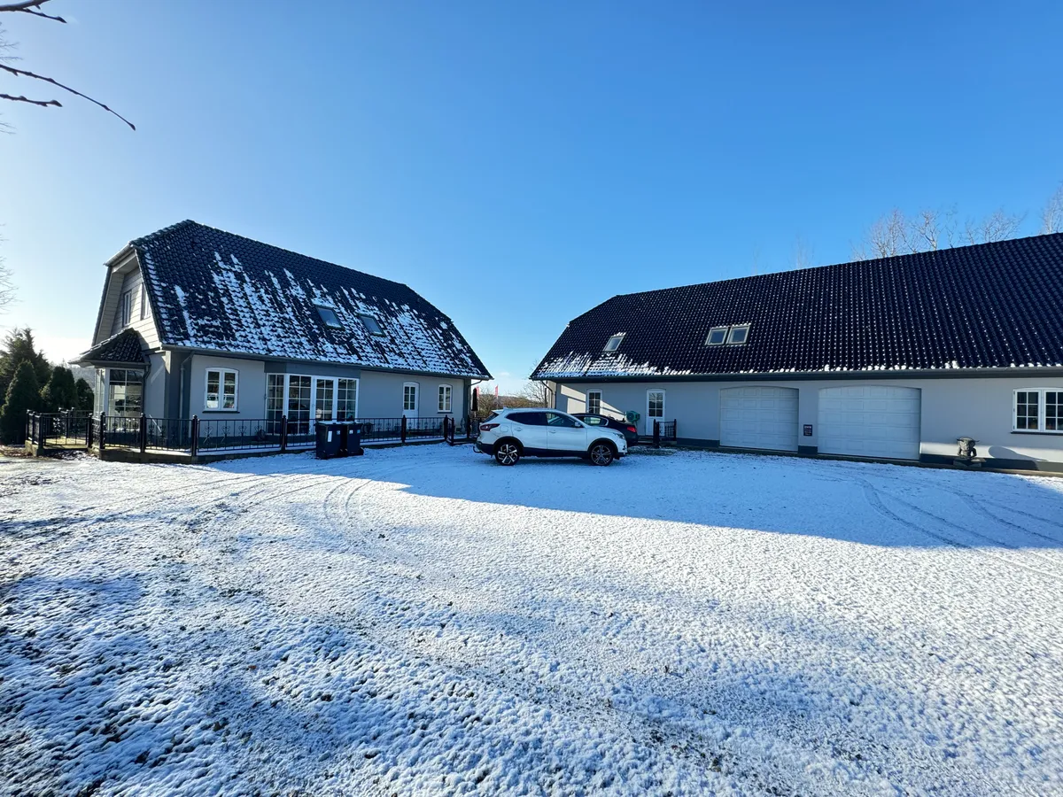 To huse med garager og en hvid bil parkeret i sneen på en solrig dag med en klar himmel og tørre træer